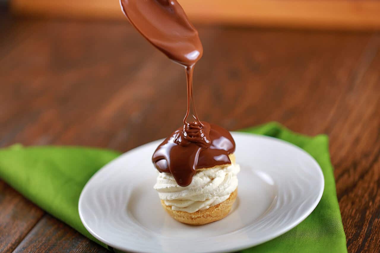 Spoon pouring chocolate whiskey sauce over top a profiterole