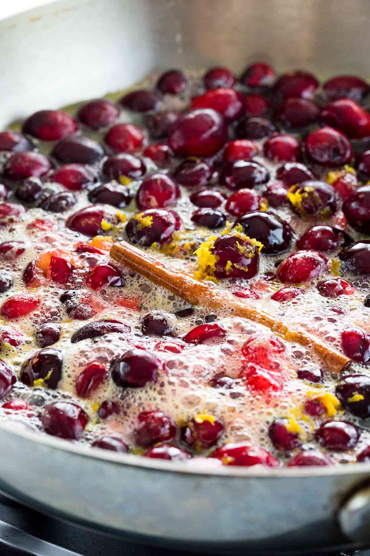 Stove top pan cooking cranberries, orange shavings with a cinnamon stick.