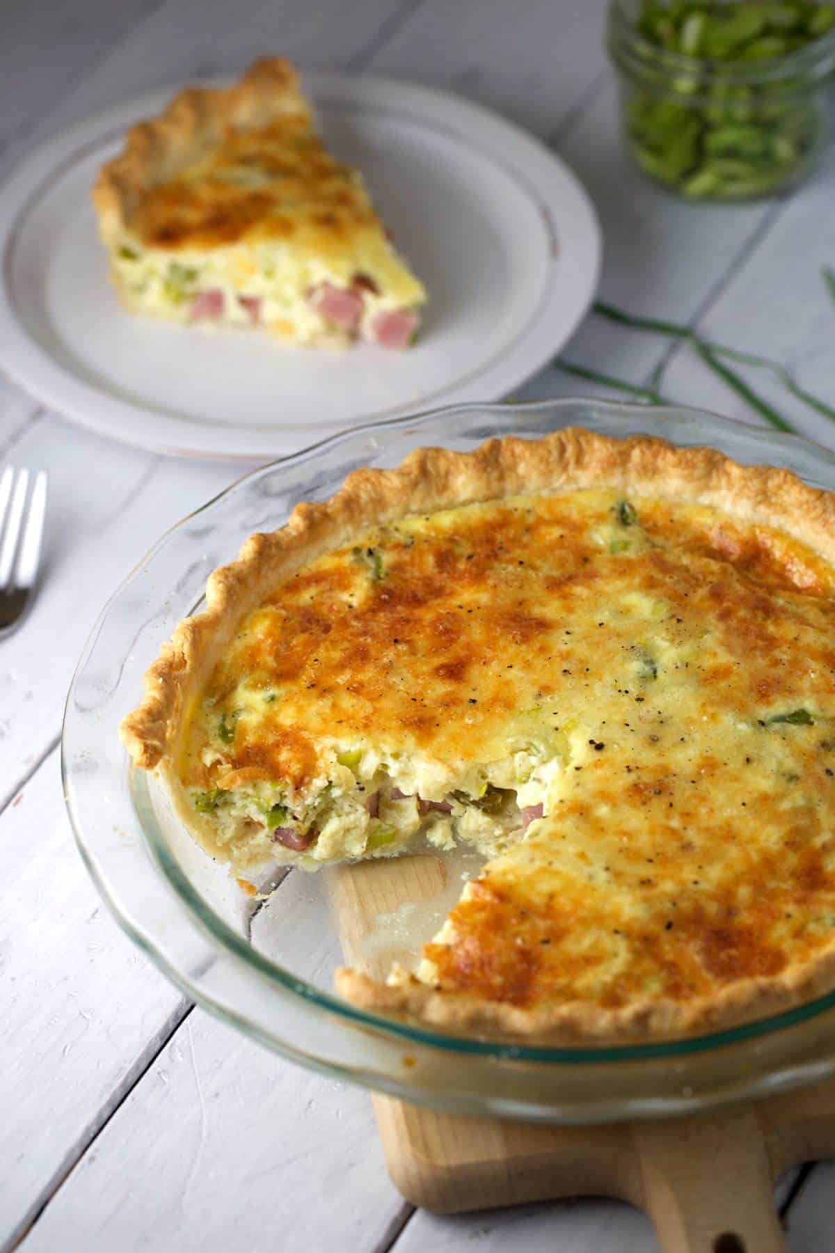 Quiche in a glass pie dish with a slice taken out of it.