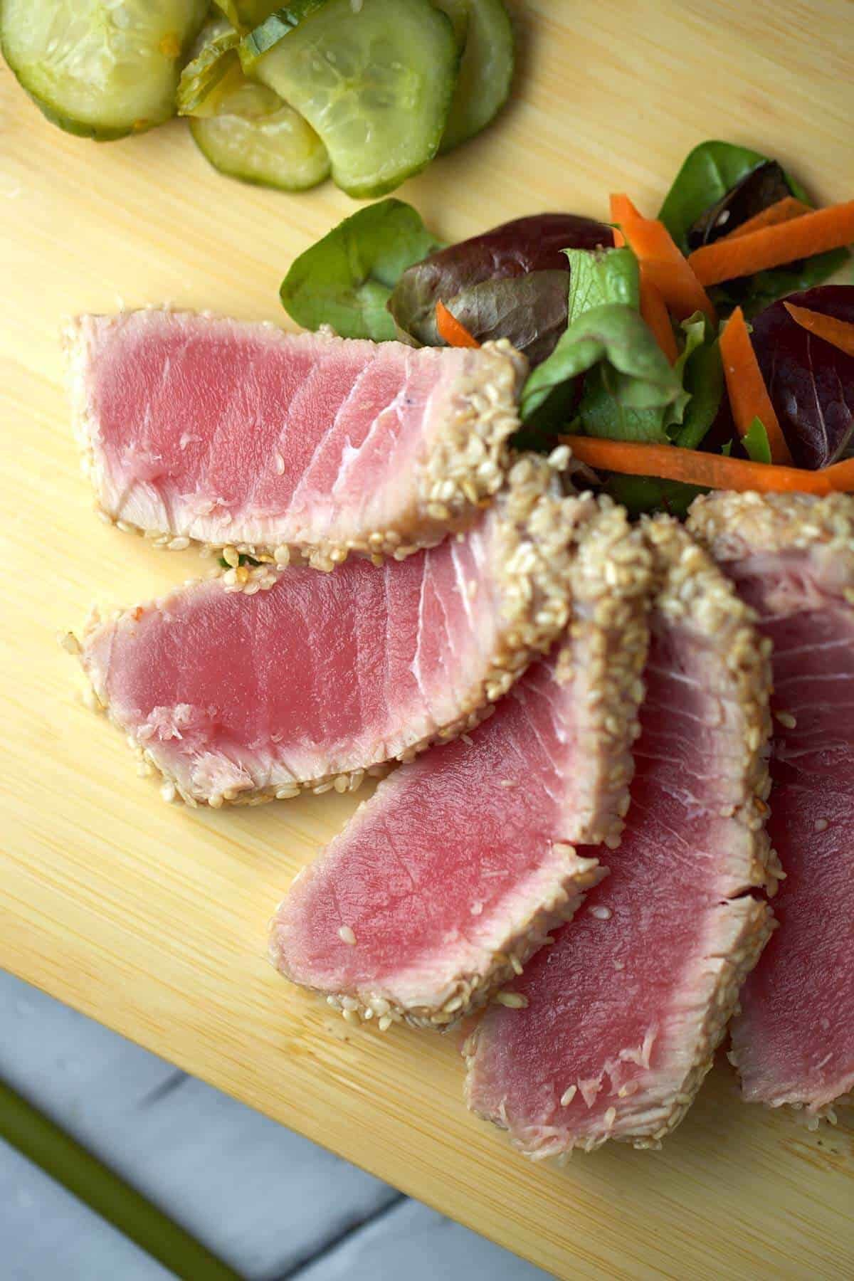 Sliced sesame-crusted ahi tuna with a seared edge and rare pink center, served with pickled cucumbers and mixed greens.