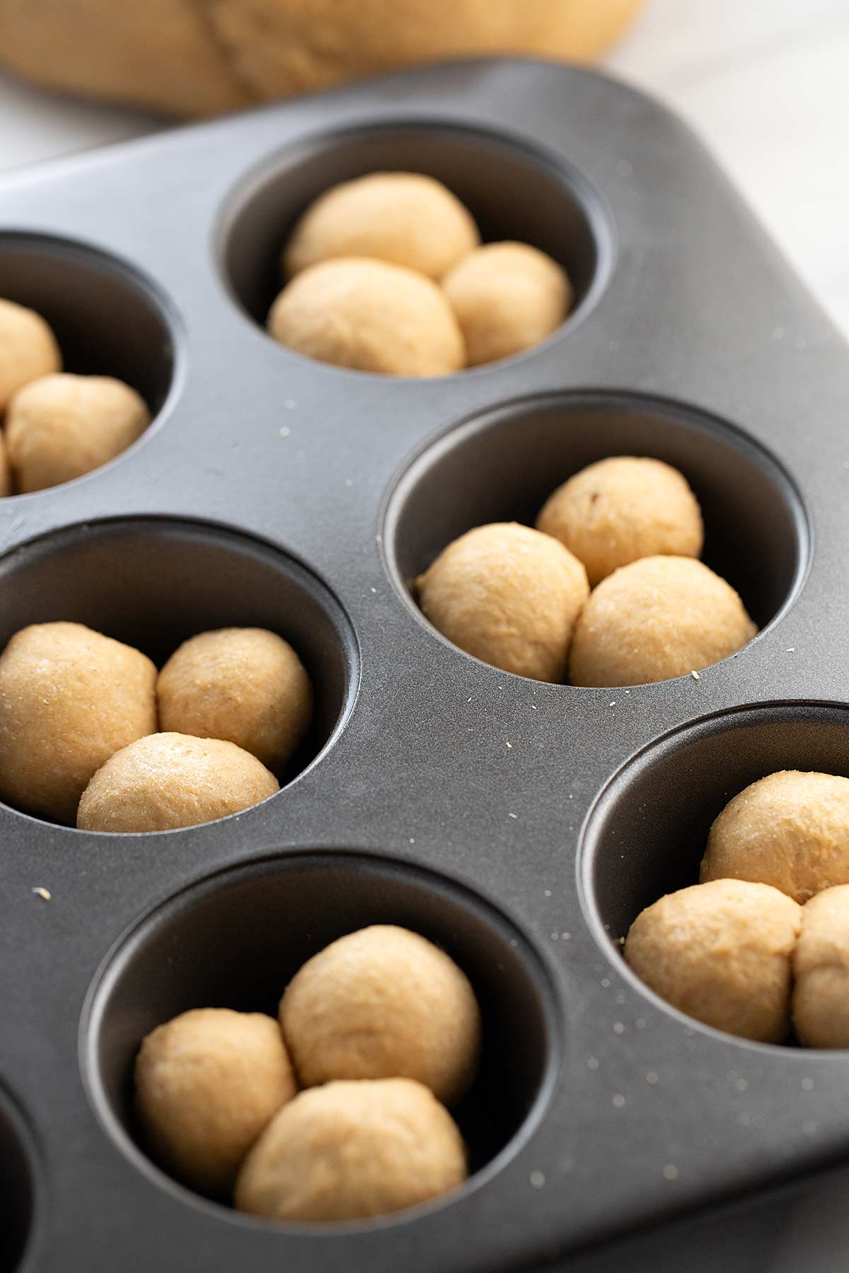 Muffin tin with 3 dough balls in each cup.