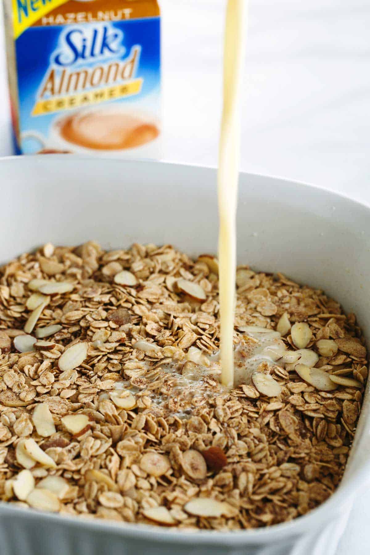 Creamer being poured into a baking dish with almond oatmeal.