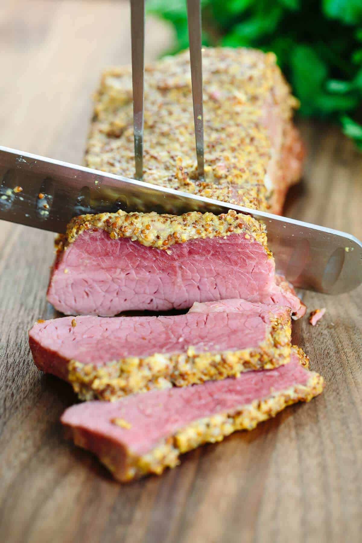 Knife slicing pieces of corned beef on a wooden cutting board.
