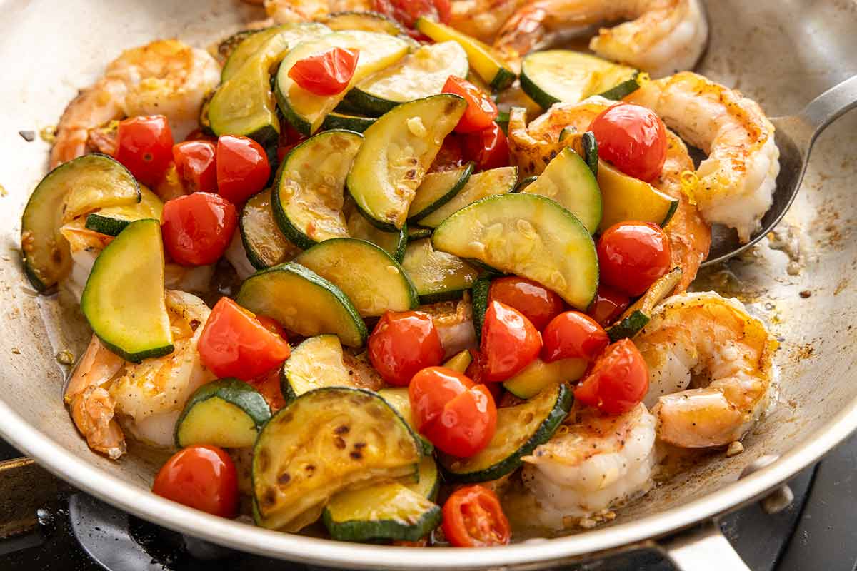 Sautéed shrimp, sliced zucchini, and halved cherry tomatoes in a skillet.