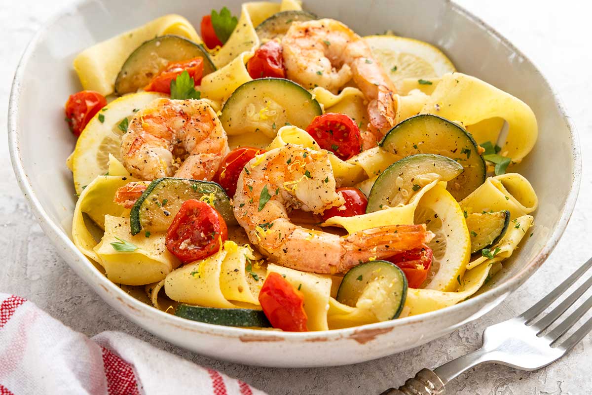 Bowl of pappardelle pasta tossed with cooked shrimp, sliced zucchini, cherry tomatoes, lemon, and parsley.