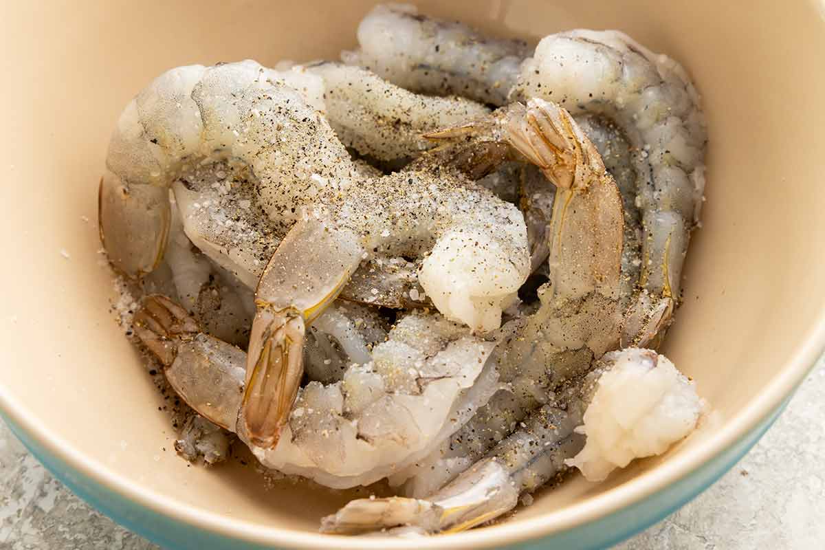 Raw peeled shrimp seasoned with salt and ground black pepper in a bowl.