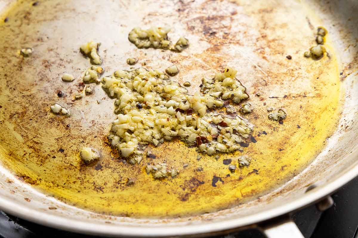 Minced garlic and red pepper flakes cooking in olive oil in a skillet.