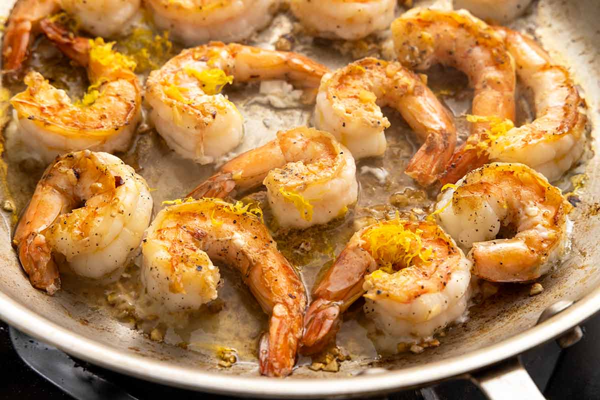 Shrimp cooking in a skillet with minced garlic, oil, and lemon zest.