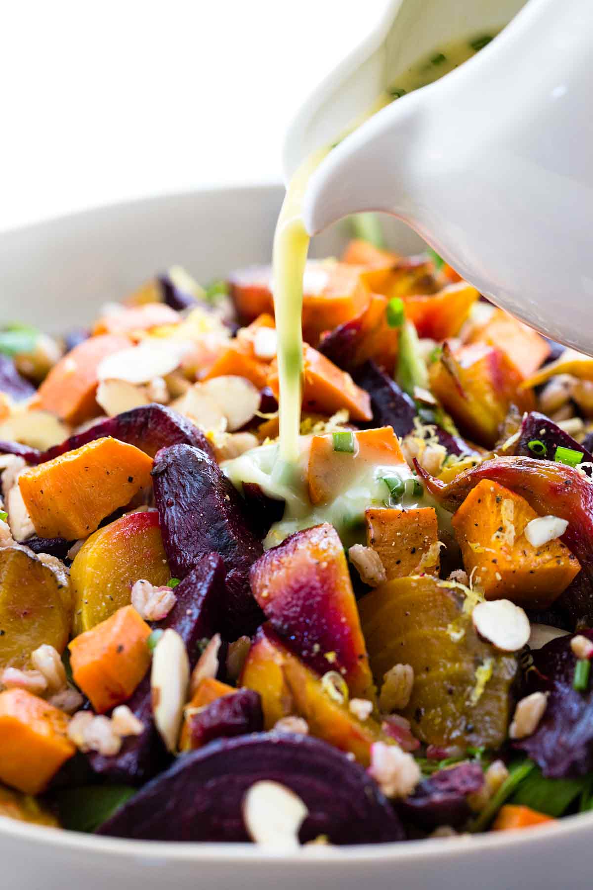 Pouring lemon garlic dressing over farro salad with root veggies.