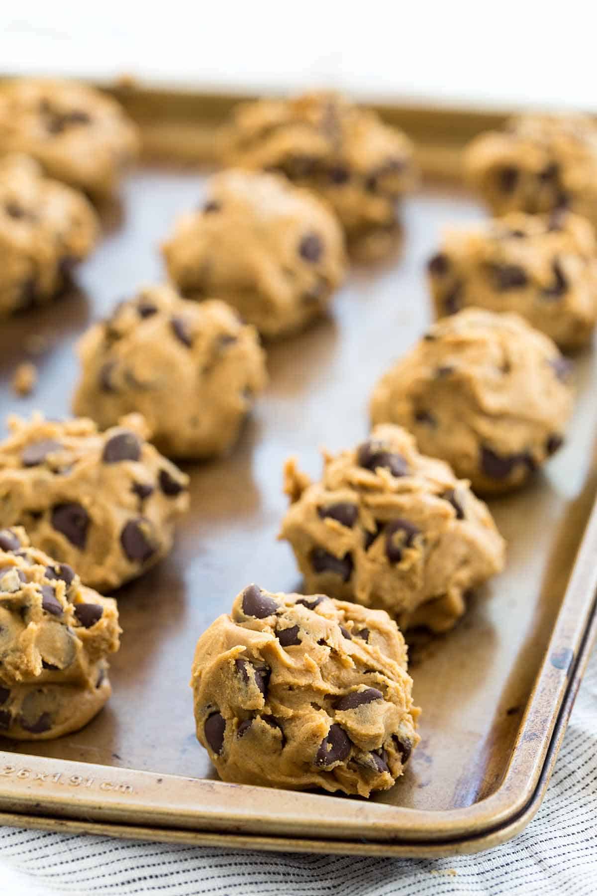 Cookie dough balls lined up on a baking sheet ready for the oven.