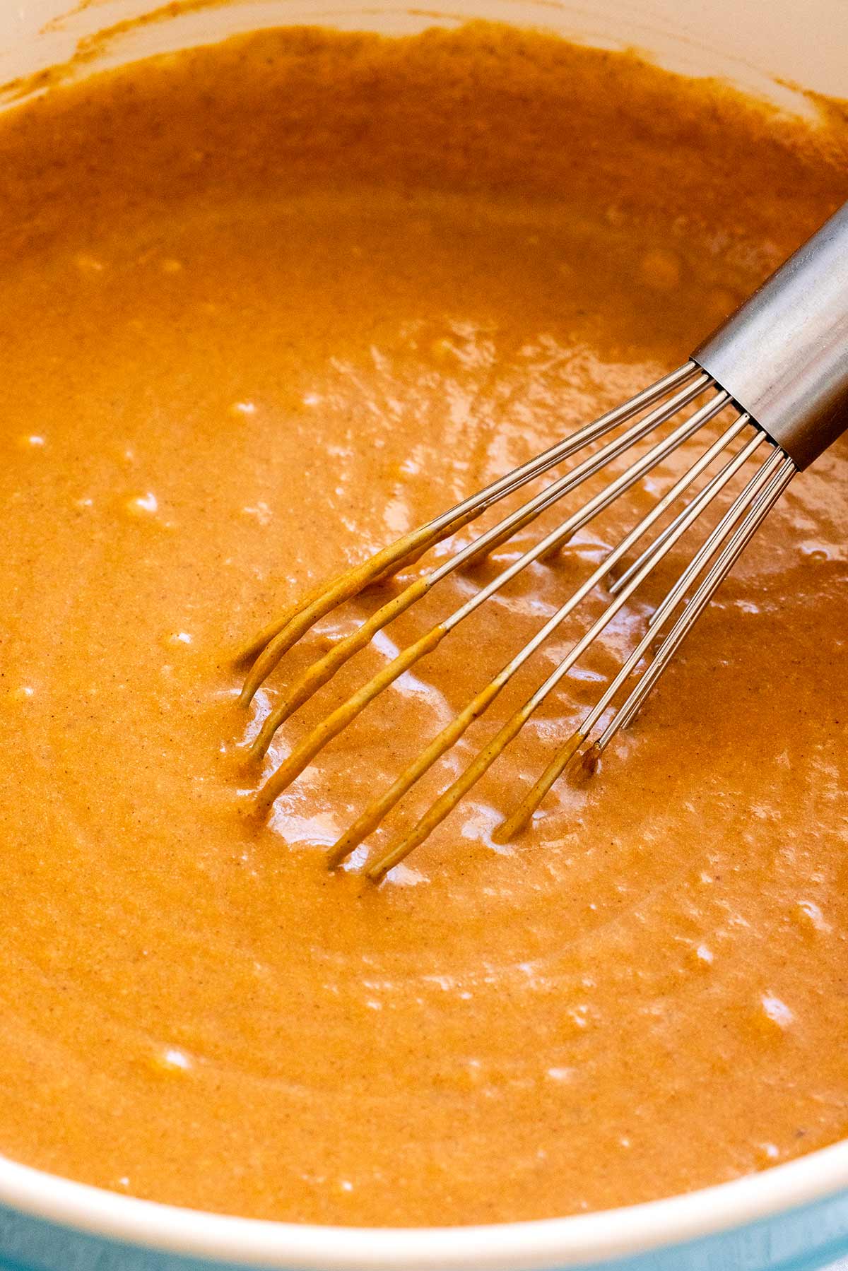 Orange pumpkin pie filling in a bowl with a whisk.