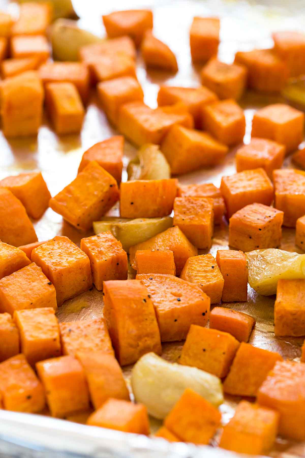 Diced sweet potatoes on a sheet pan with sliced garlic.