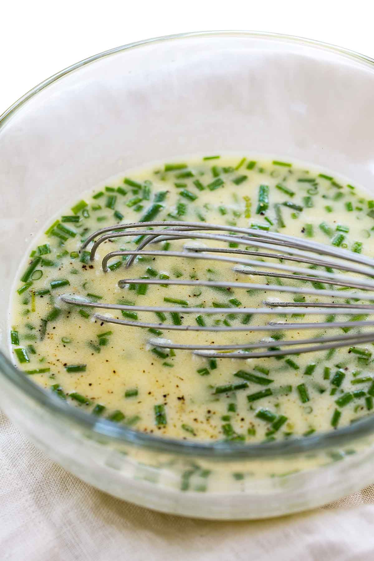 Whisking a bowl of lemon garlic dressing with sliced green chives.