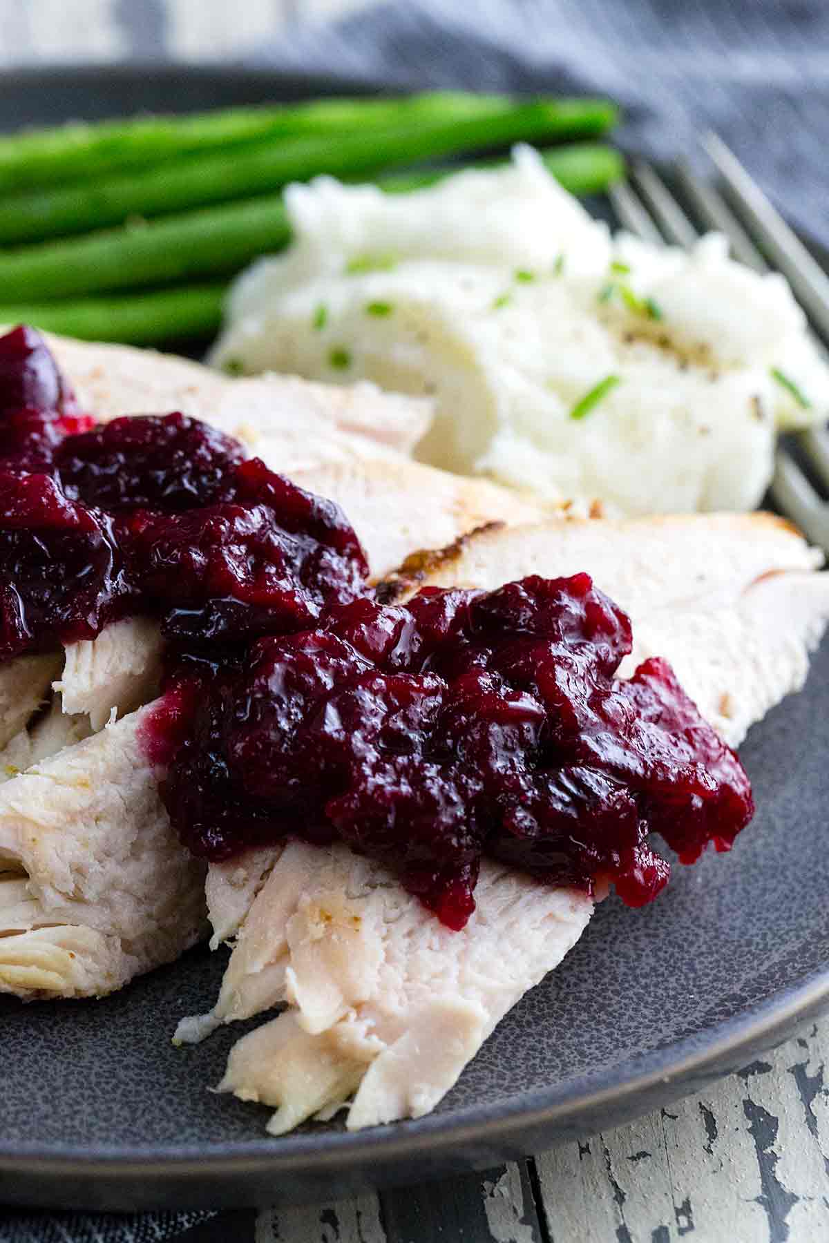 A dinner plate with cranberry sauce placed over white meat chicken.