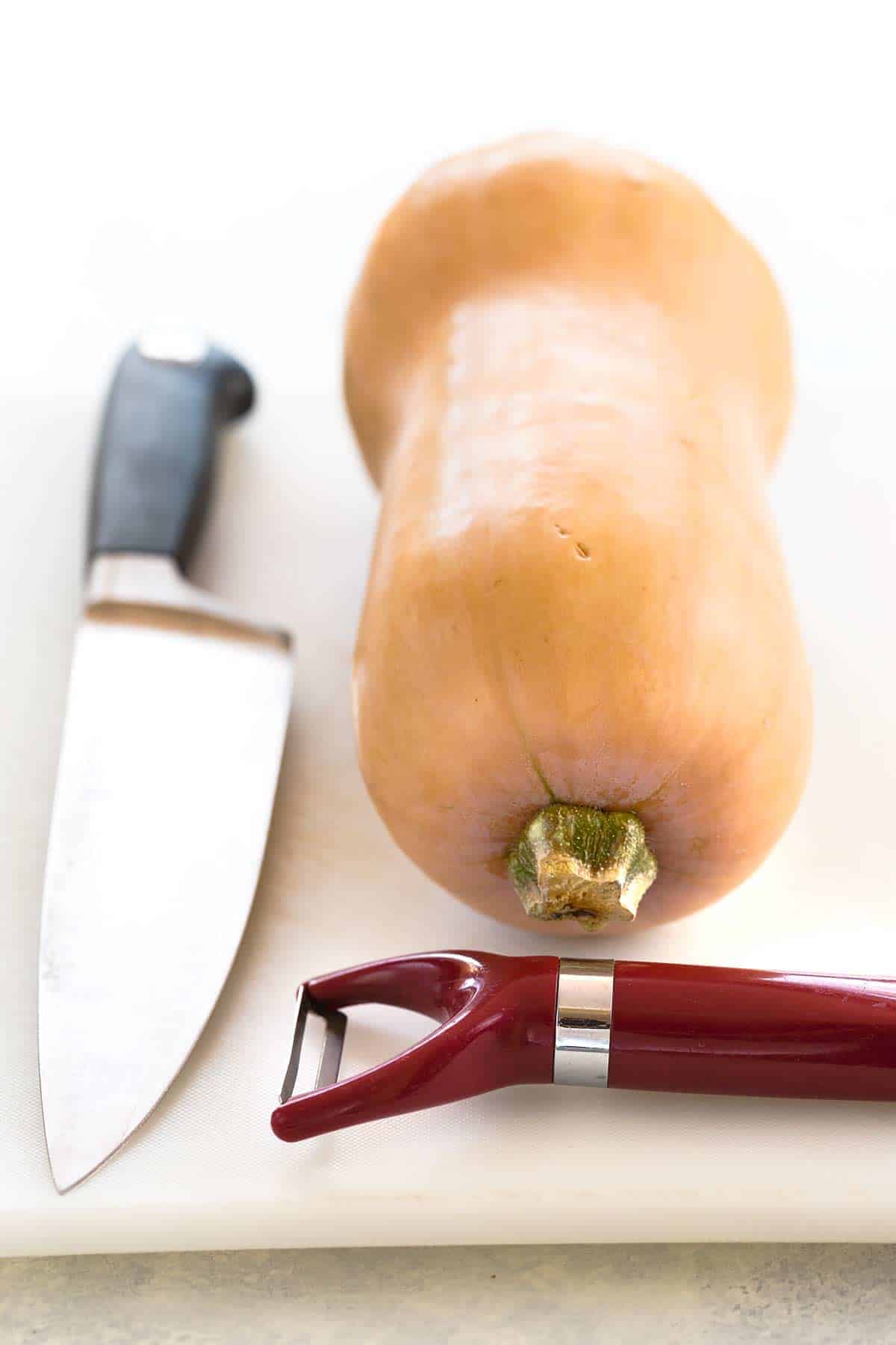 Cutting board with chef knife, peeler, and an uncut butternut squash.