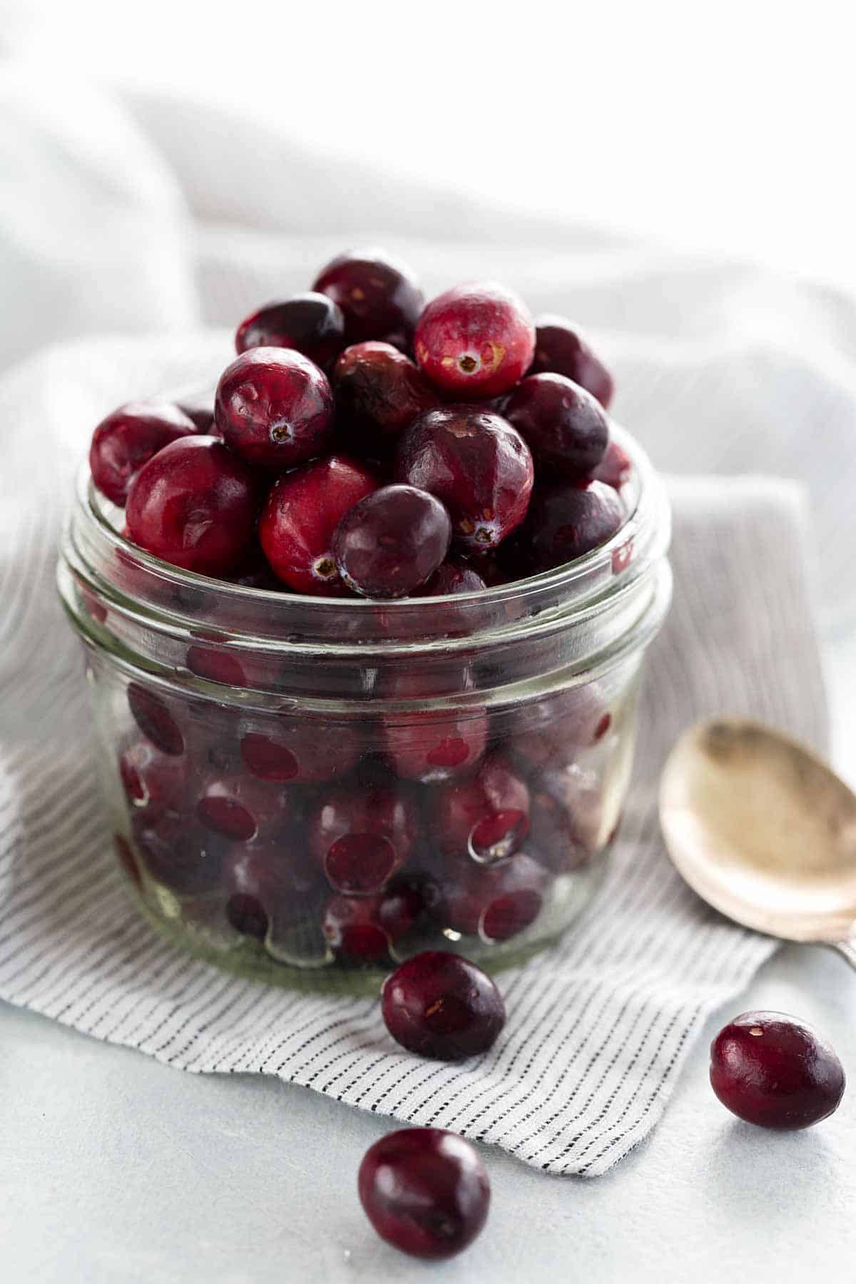 A clear mason jar overfilled with cranberries.