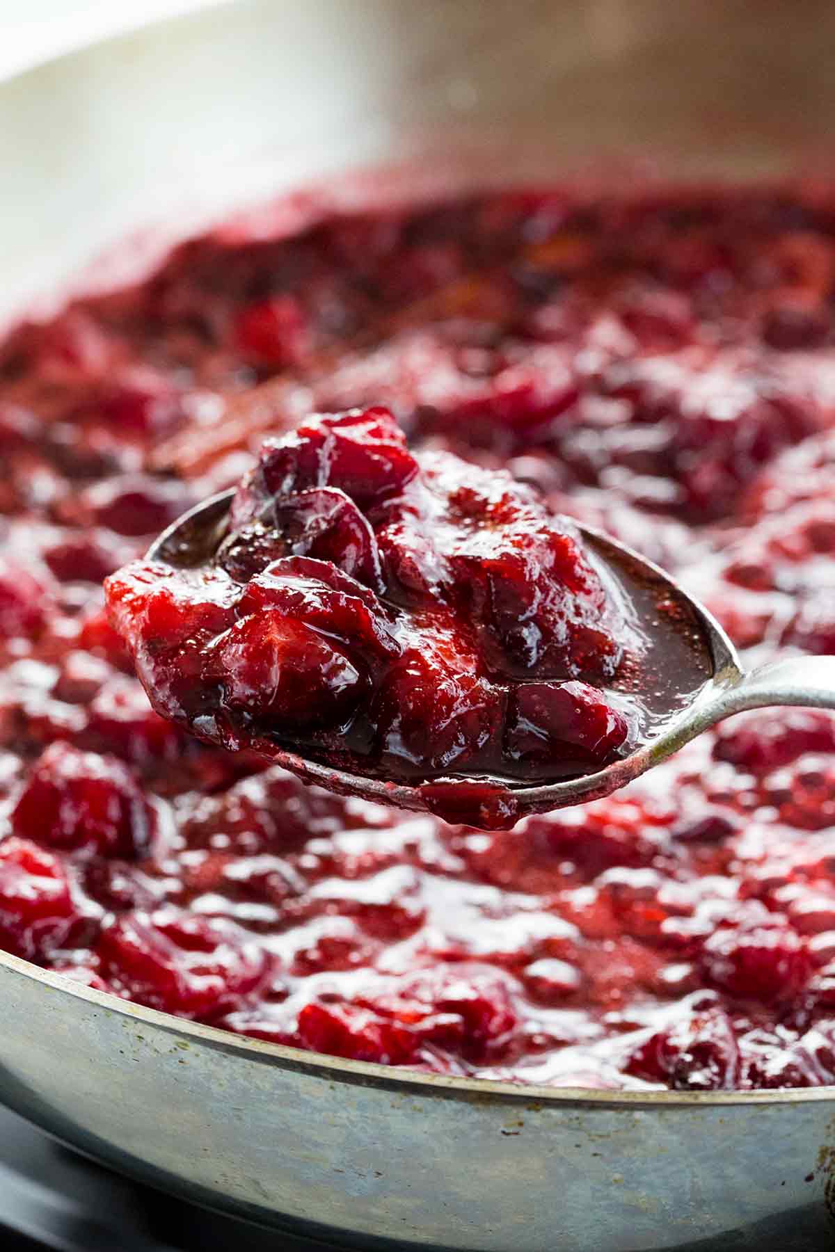 Spoon picking up a scoop of homemade orange cranberry sauce from a pan.