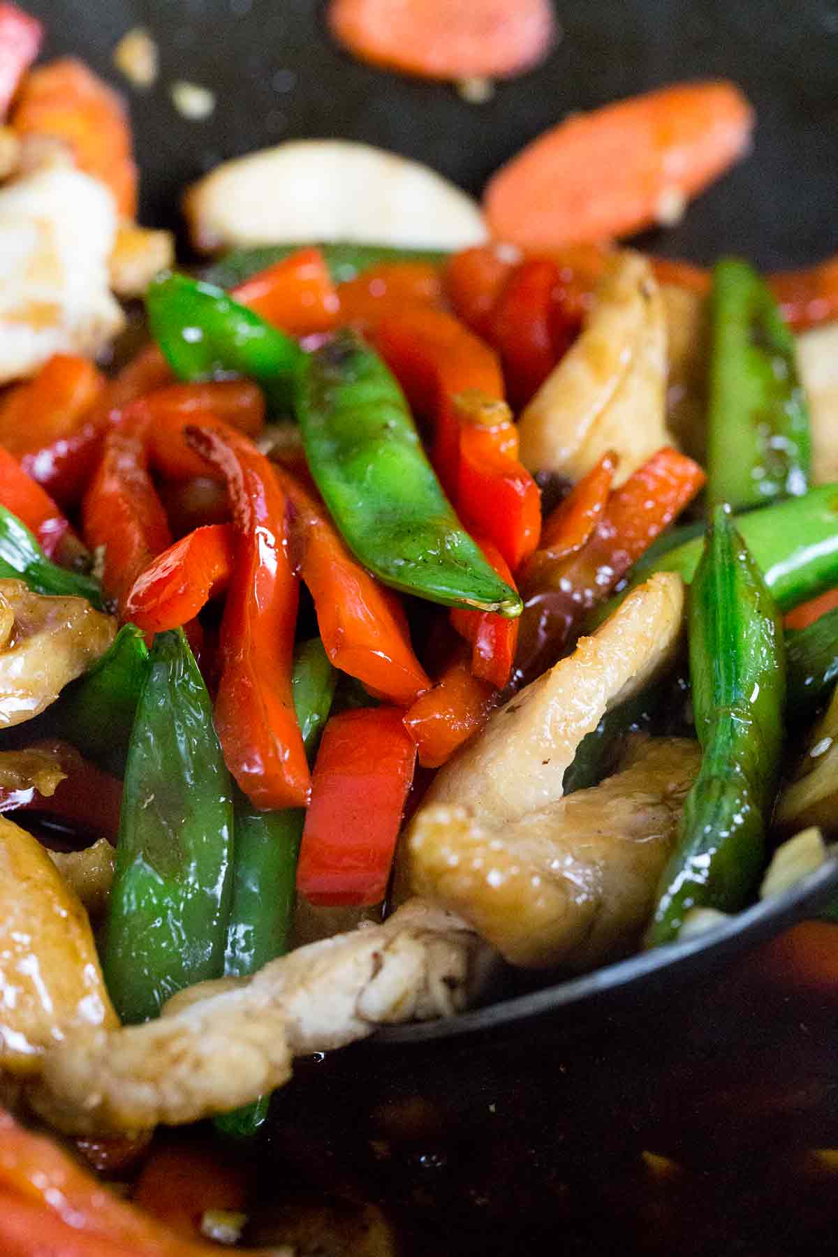 Chicken, carrots, snap peas, and red peppers being tossed together in a wok.