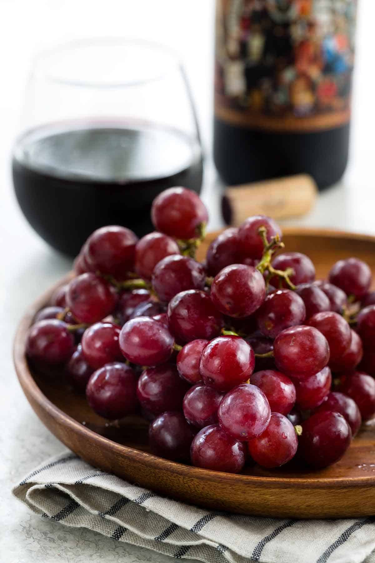Red grapes on a wooden plate with a glass of red wine in the background.