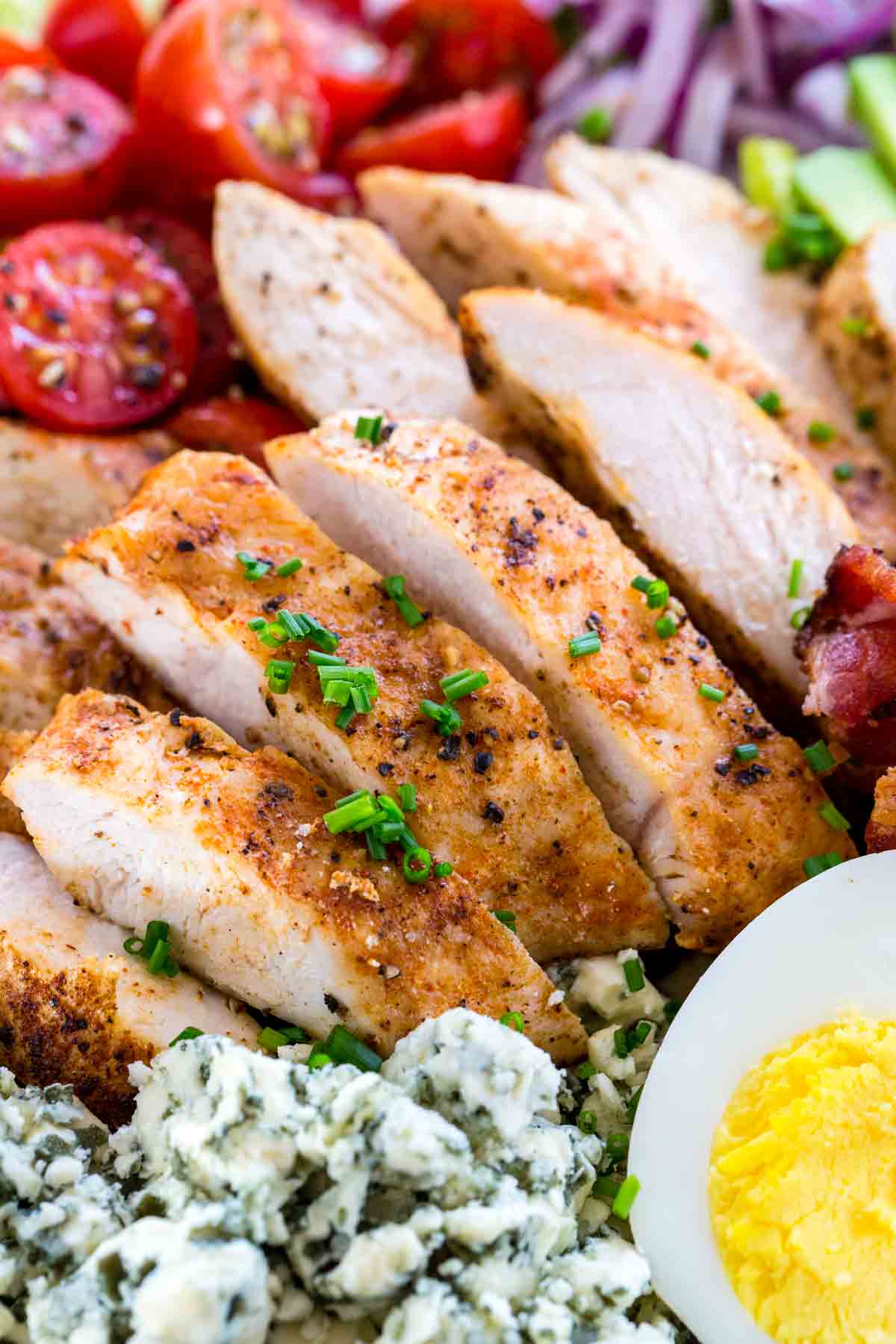 Close up of sliced chicken breast with tomatoes and eggs.