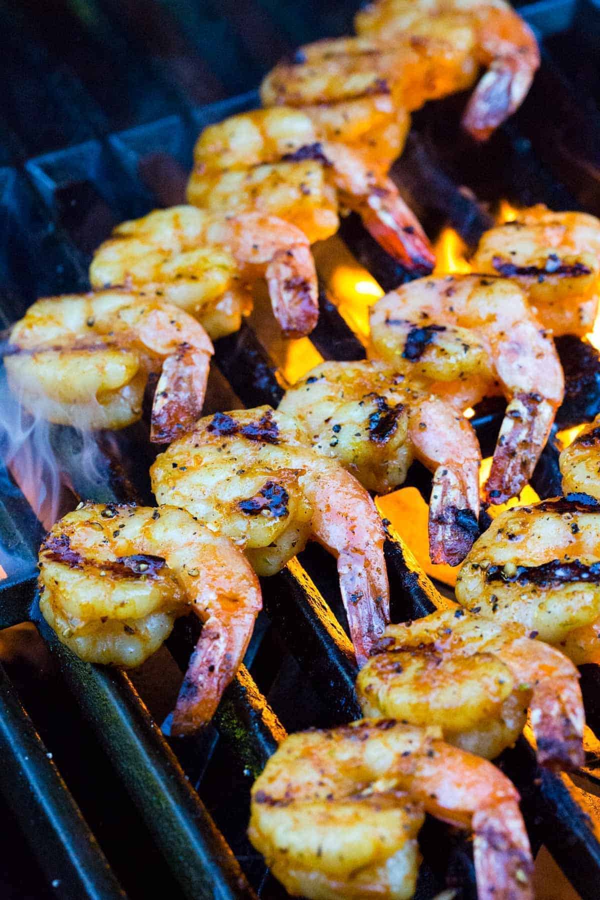 Seasoned shrimp skewers cooking directly over open flames on a grill, with charred grill marks forming.