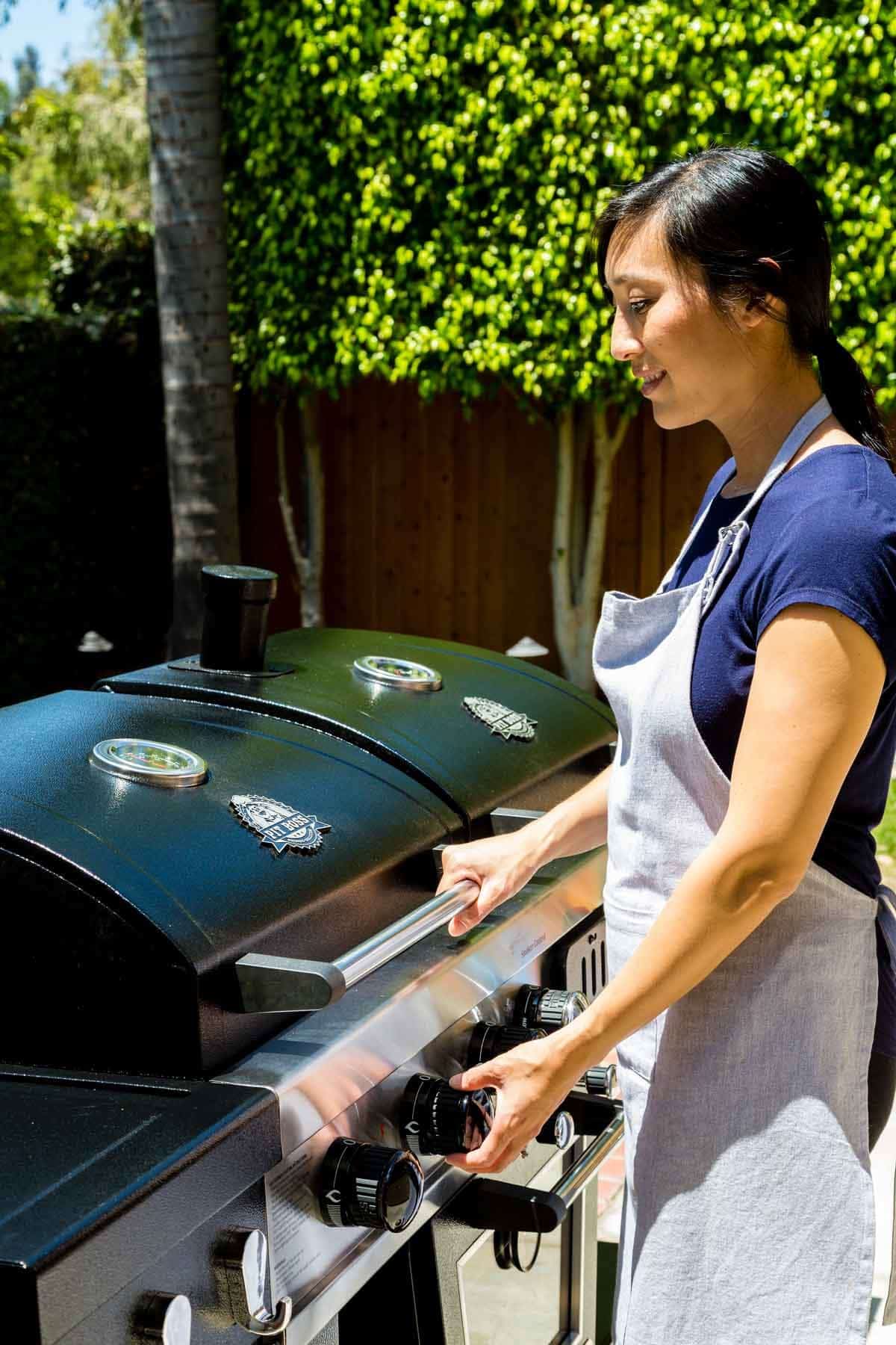 Woman in an apron adjusting the control knobs on the Pit Boss Memphis Ultimate grill outdoors.