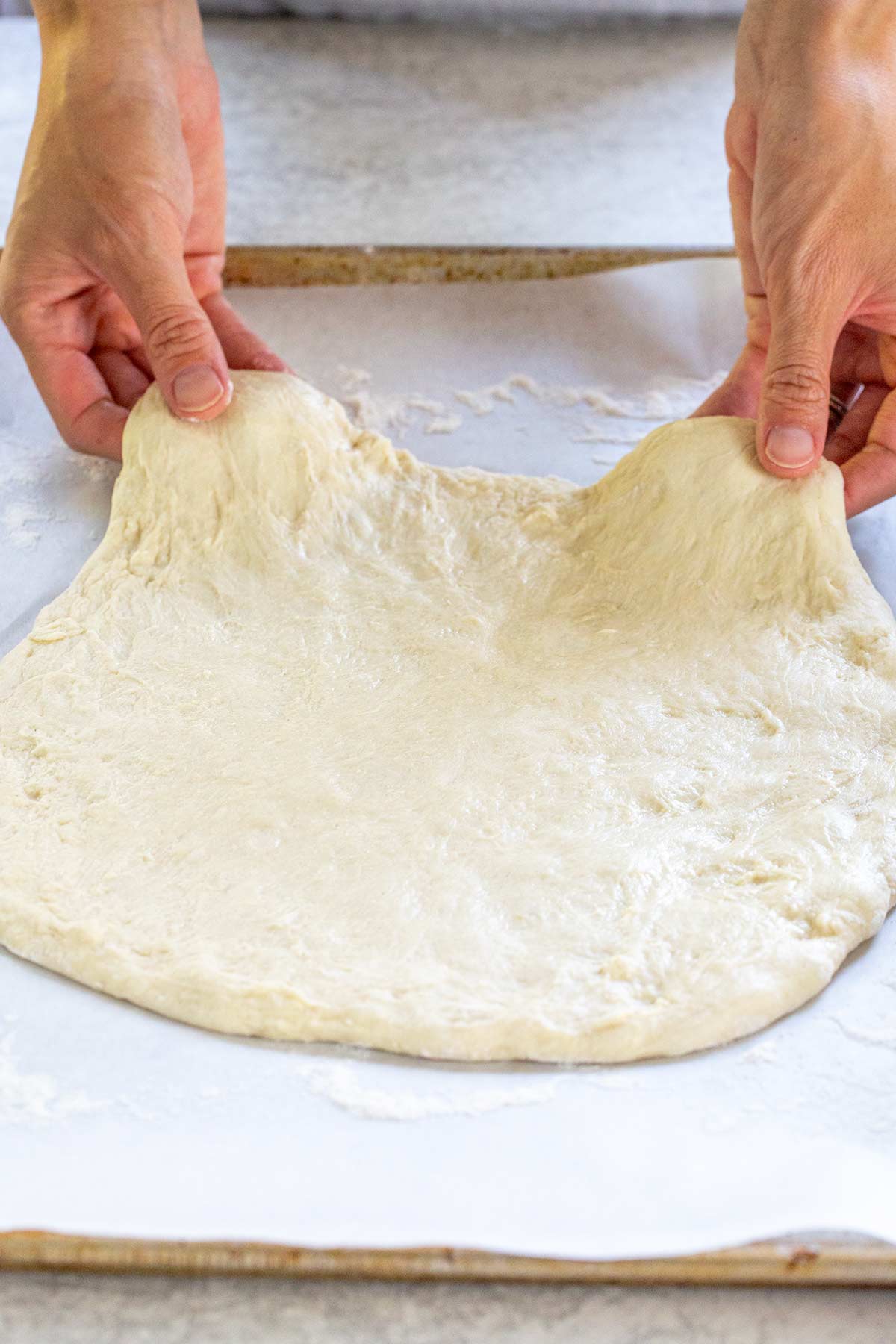 Hands gently stretching pizza dough into a round shape on floured parchment paper.