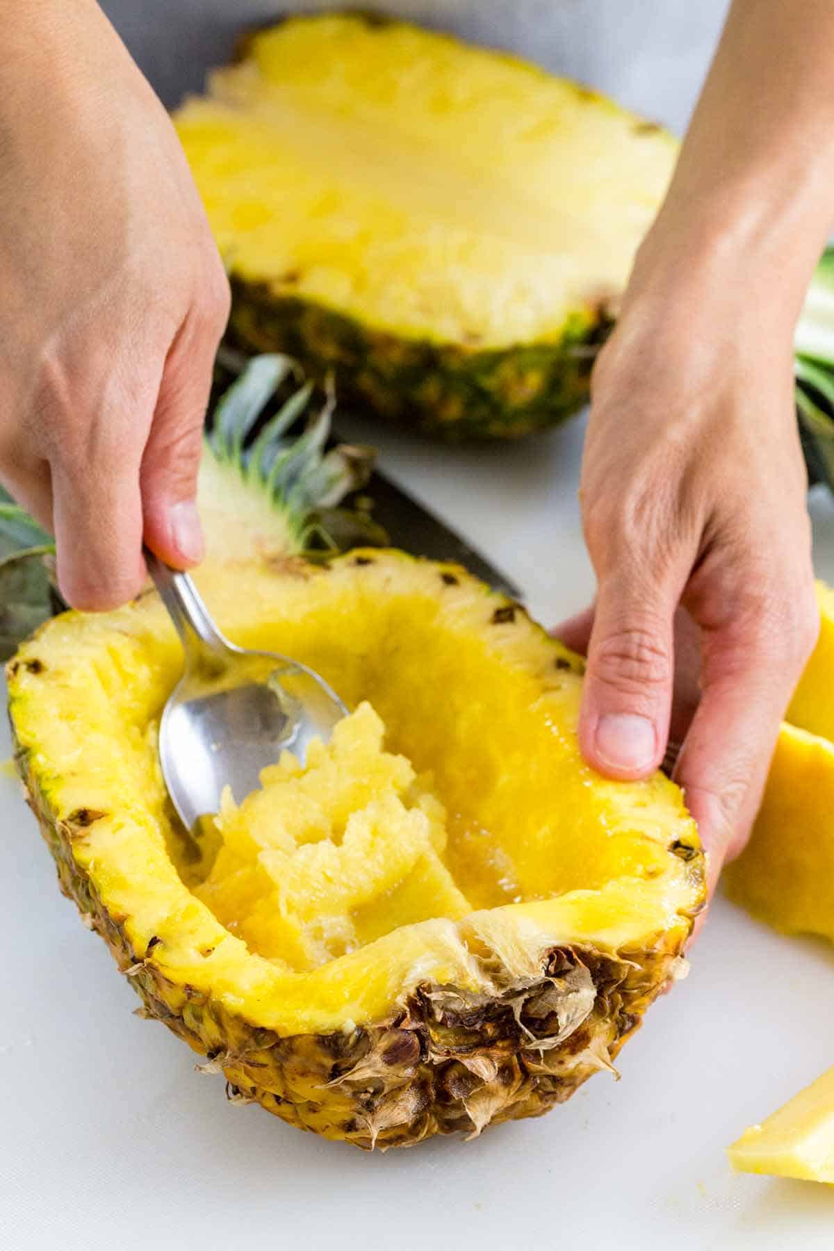 Person carving out a pineapple bowl to serve food in.