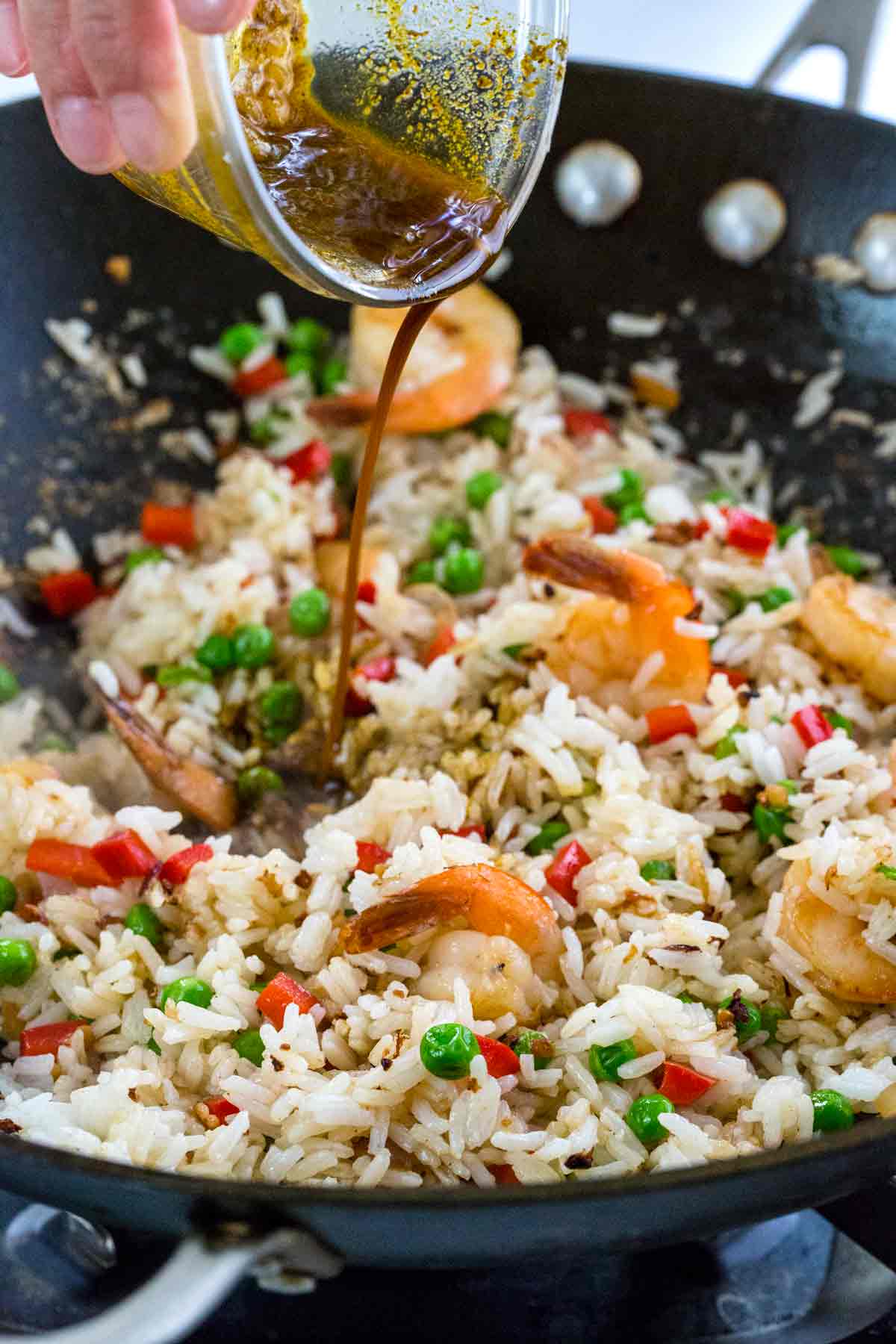 Pouring stir fry sauce into a wok with rice and shrimp.