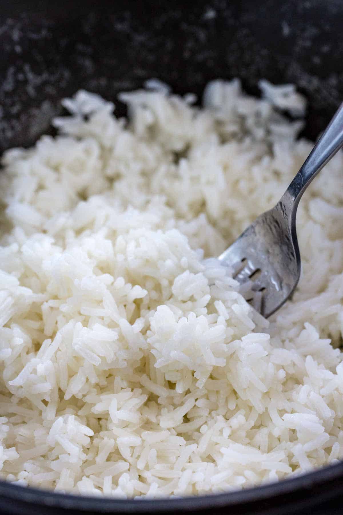 Jasmin rice cooking in a pot with a fork fluffing the rice.