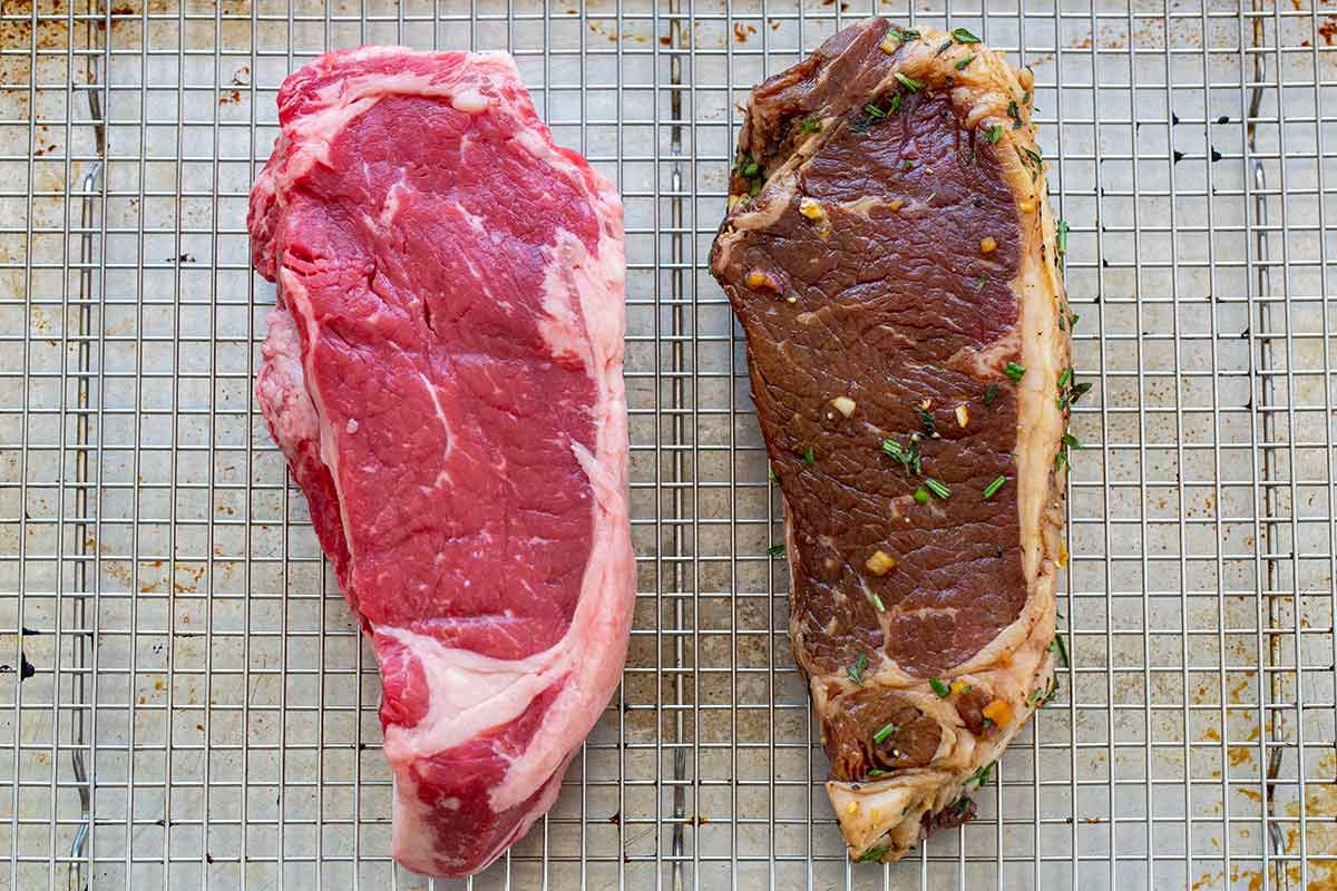 Side-by-side comparison of a bright red raw steak and a darker marinated steak with herbs on a wire rack.