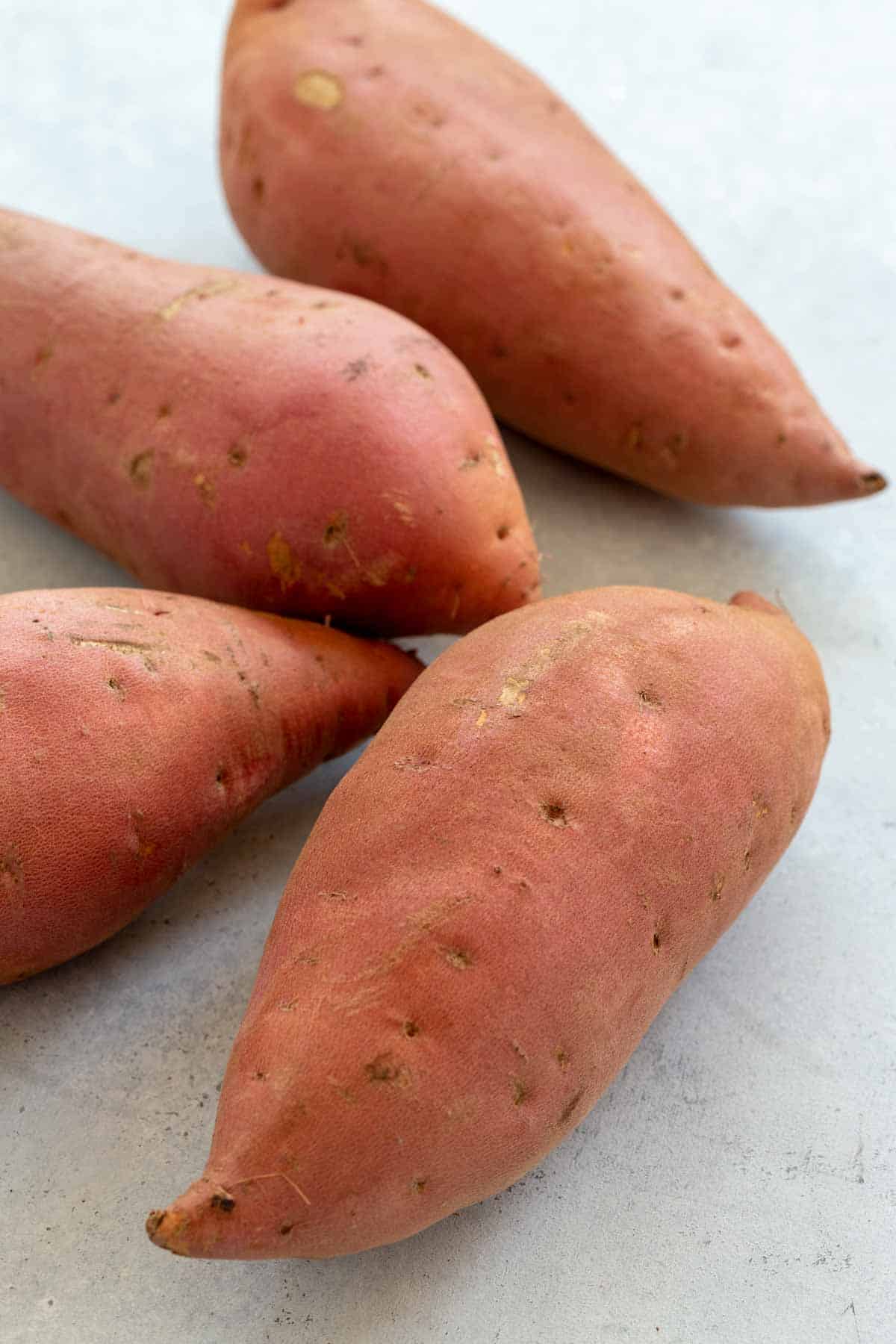 Four uncooked sweet potatoes on a cutting board.