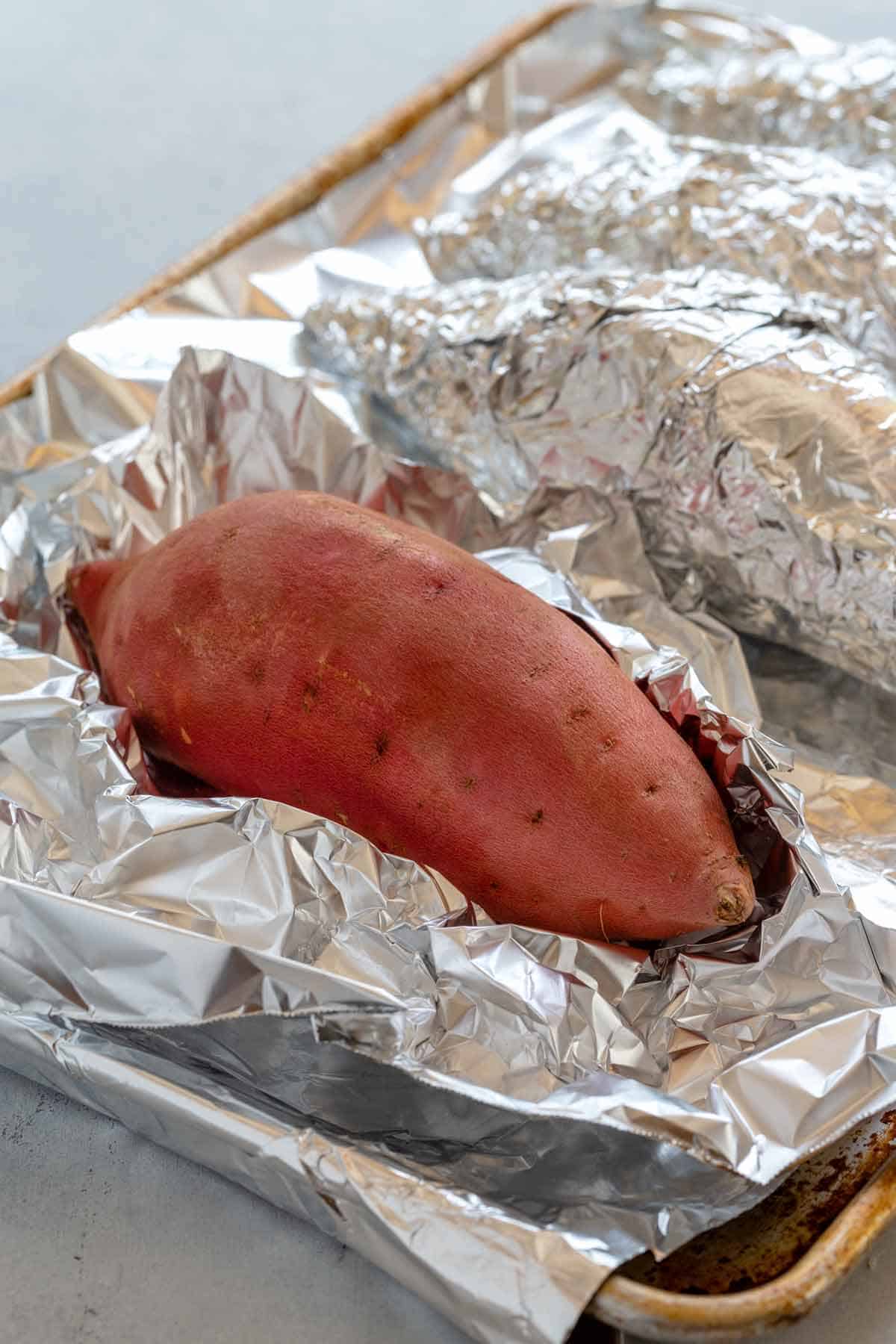 Sweet potatoes in the process of being wrapped in foil and placed on a sheet pan.