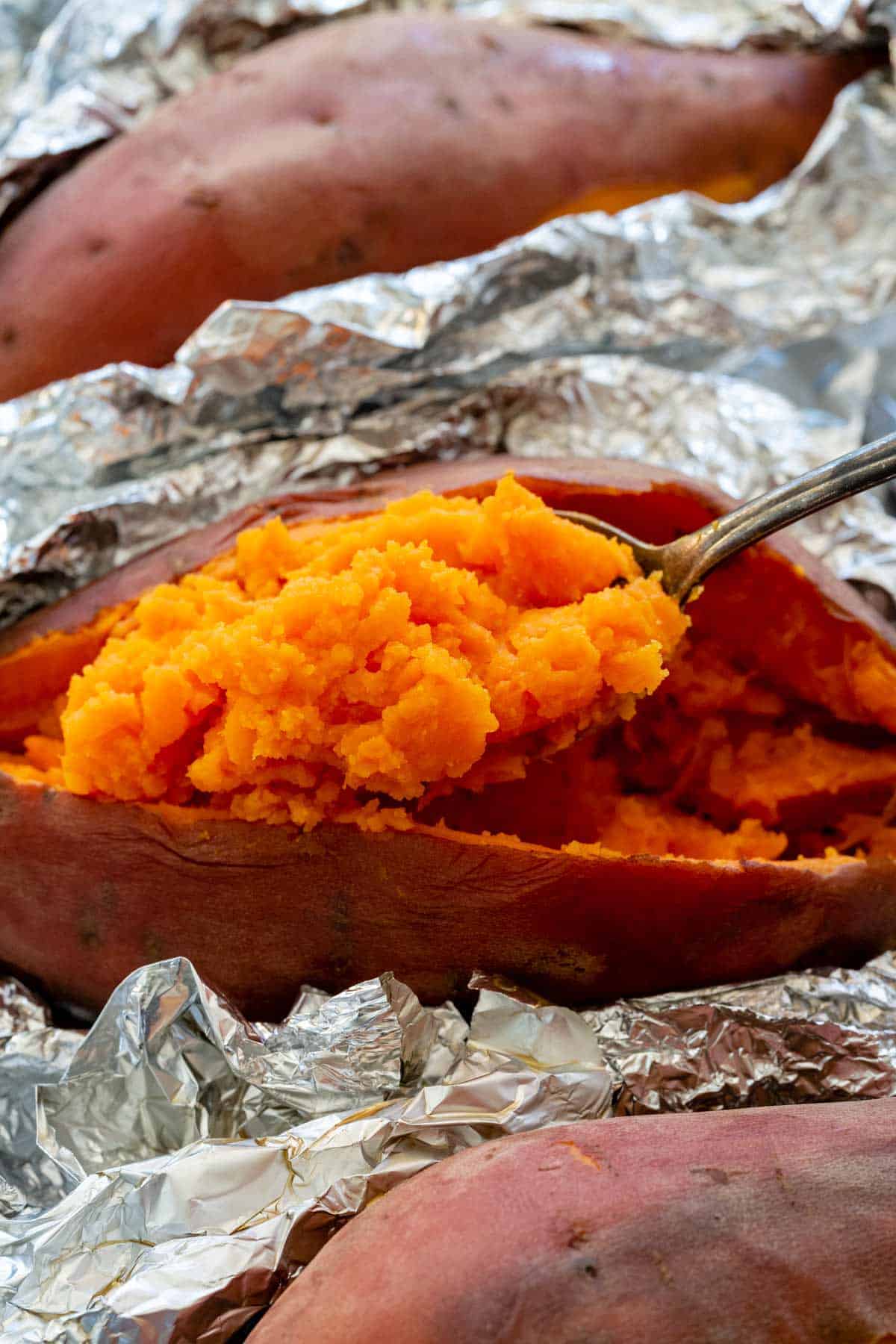 Fork scooping the insides of a baked sweet potato.