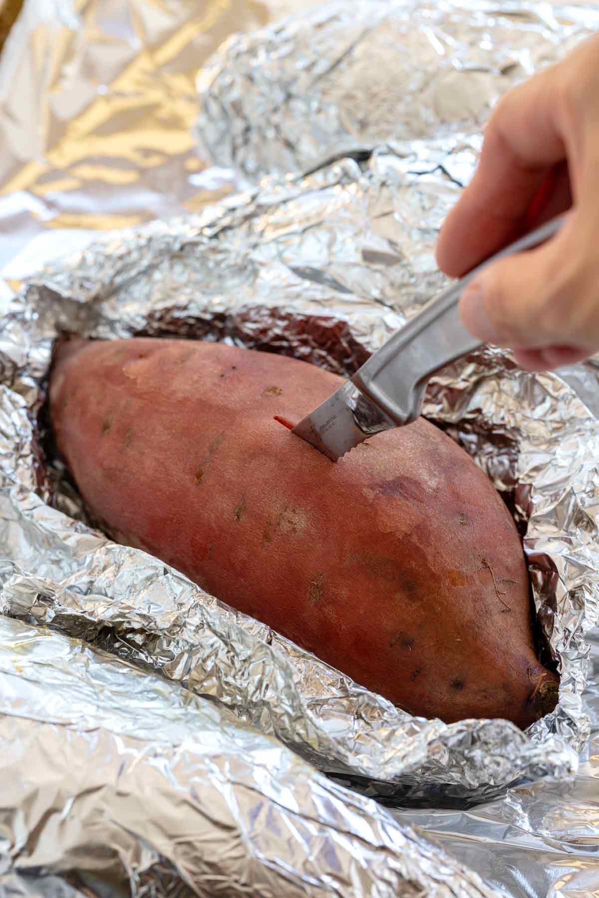 Piercing a knife into a baked sweet potato to check for doneness.