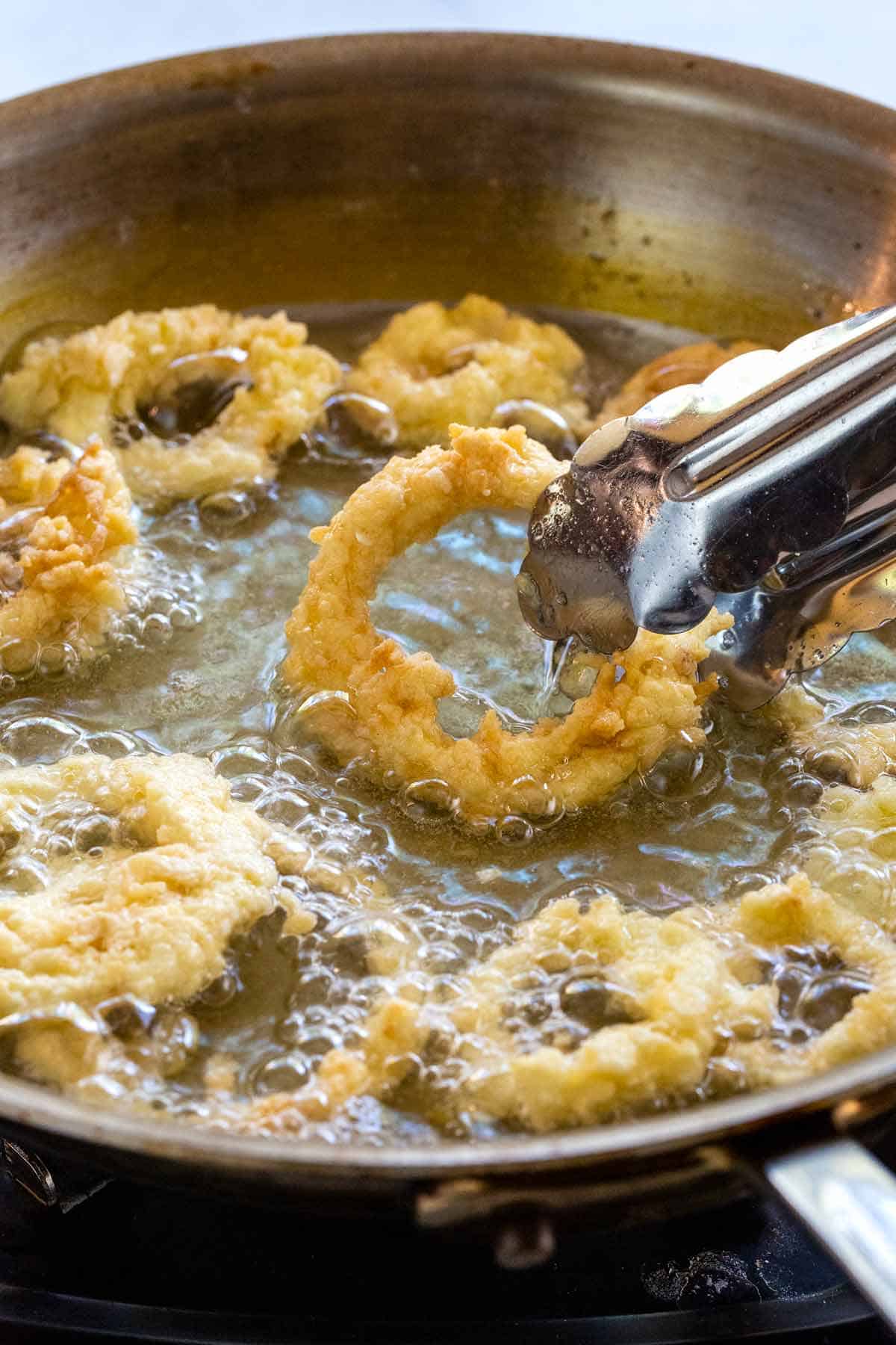 Homemade onion rings frying in a pan.