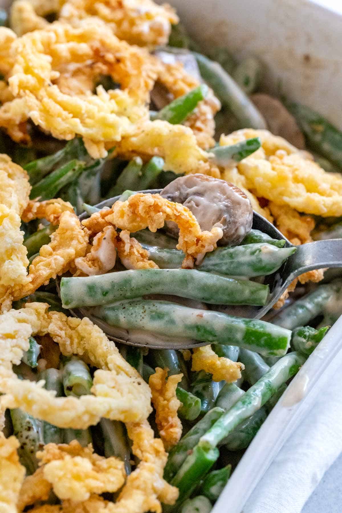 Spoon serving green beans and onion rings from a casserole dish.