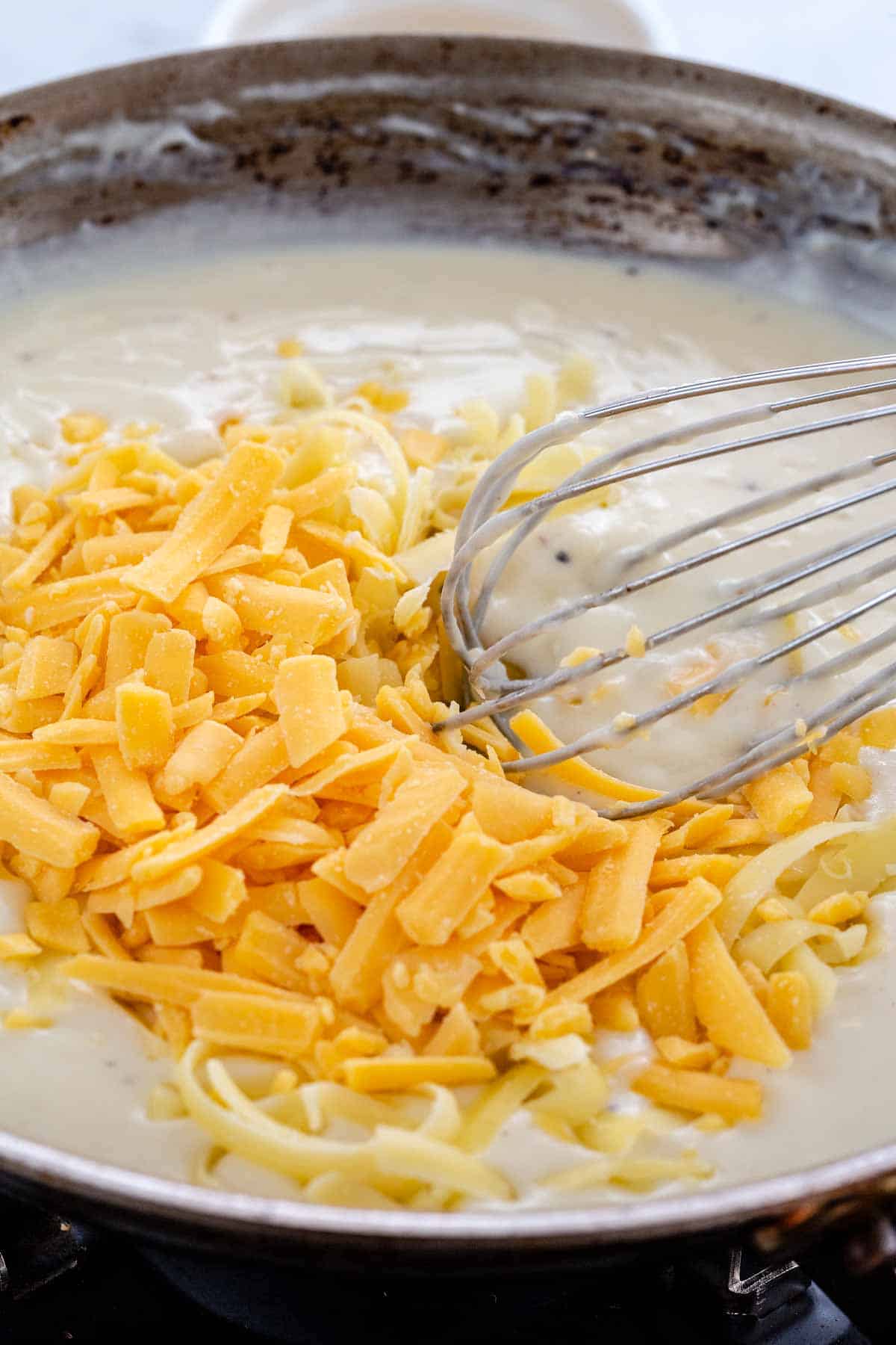 Two types of cheeses being whisked into a roux-based pan sauce.
