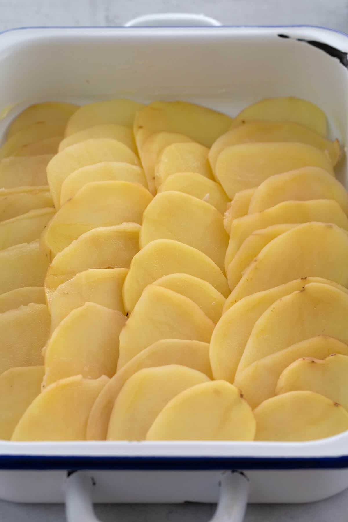 Sliced potatoes lined up in a casserole dish.