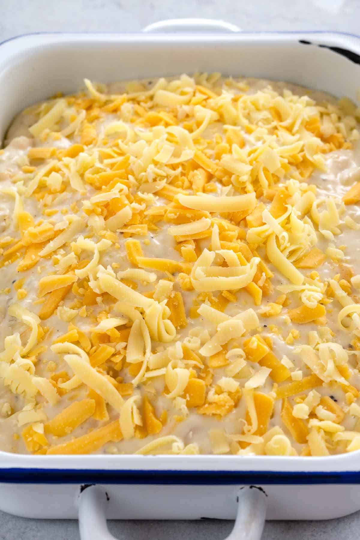 Grated pieces of gruyere and sharp cheddar cheese sprinkled on top of uncooked potatoes au gratin casserole.