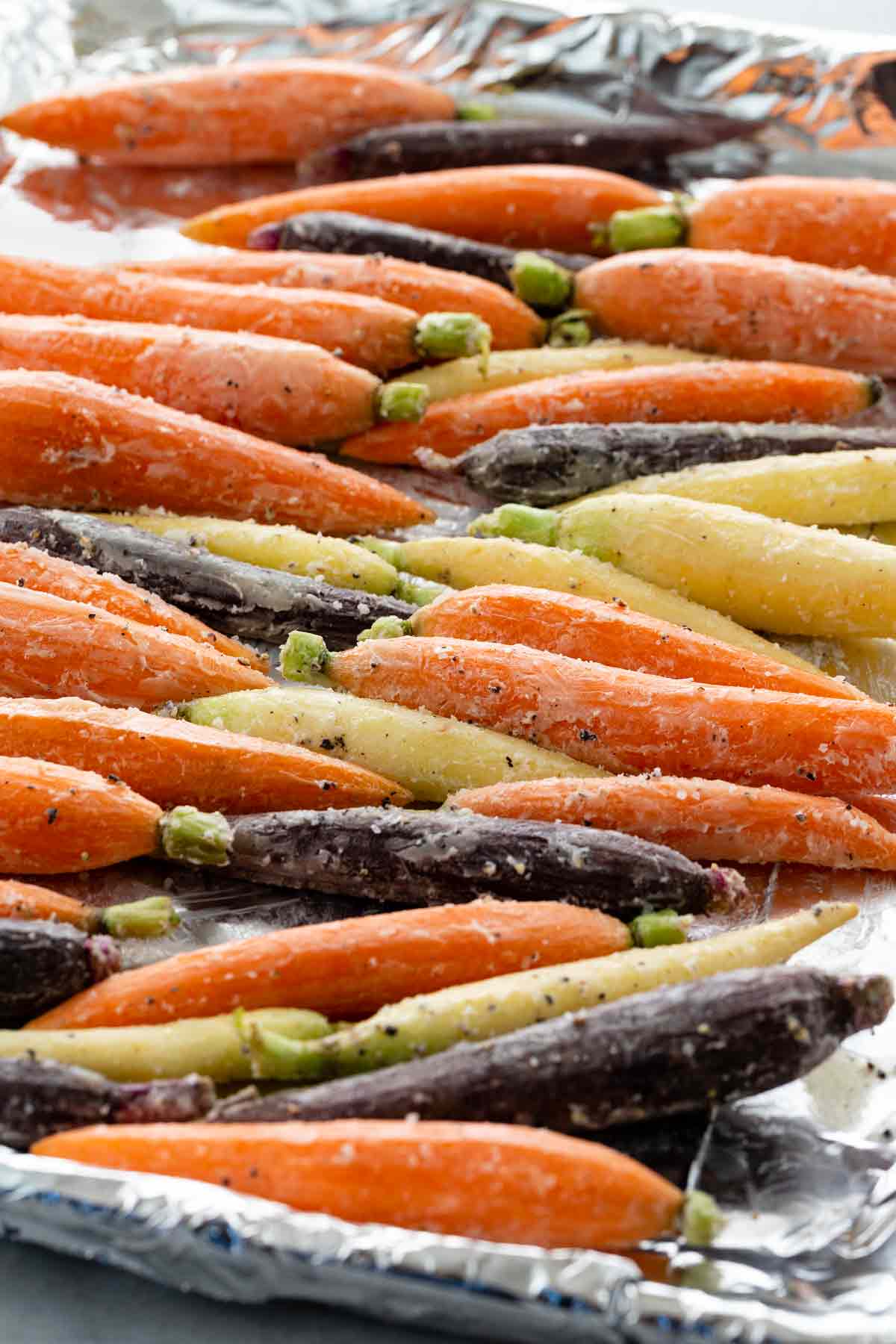 Seasoned carrots lined up on a foil-lined baking sheet.