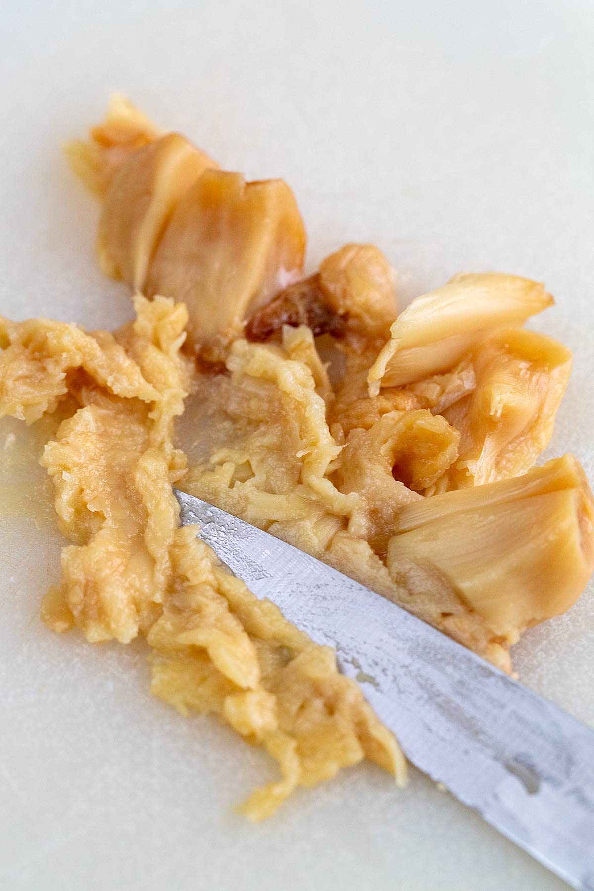 Flat side of a knife pressing roasted garlic into a paste.
