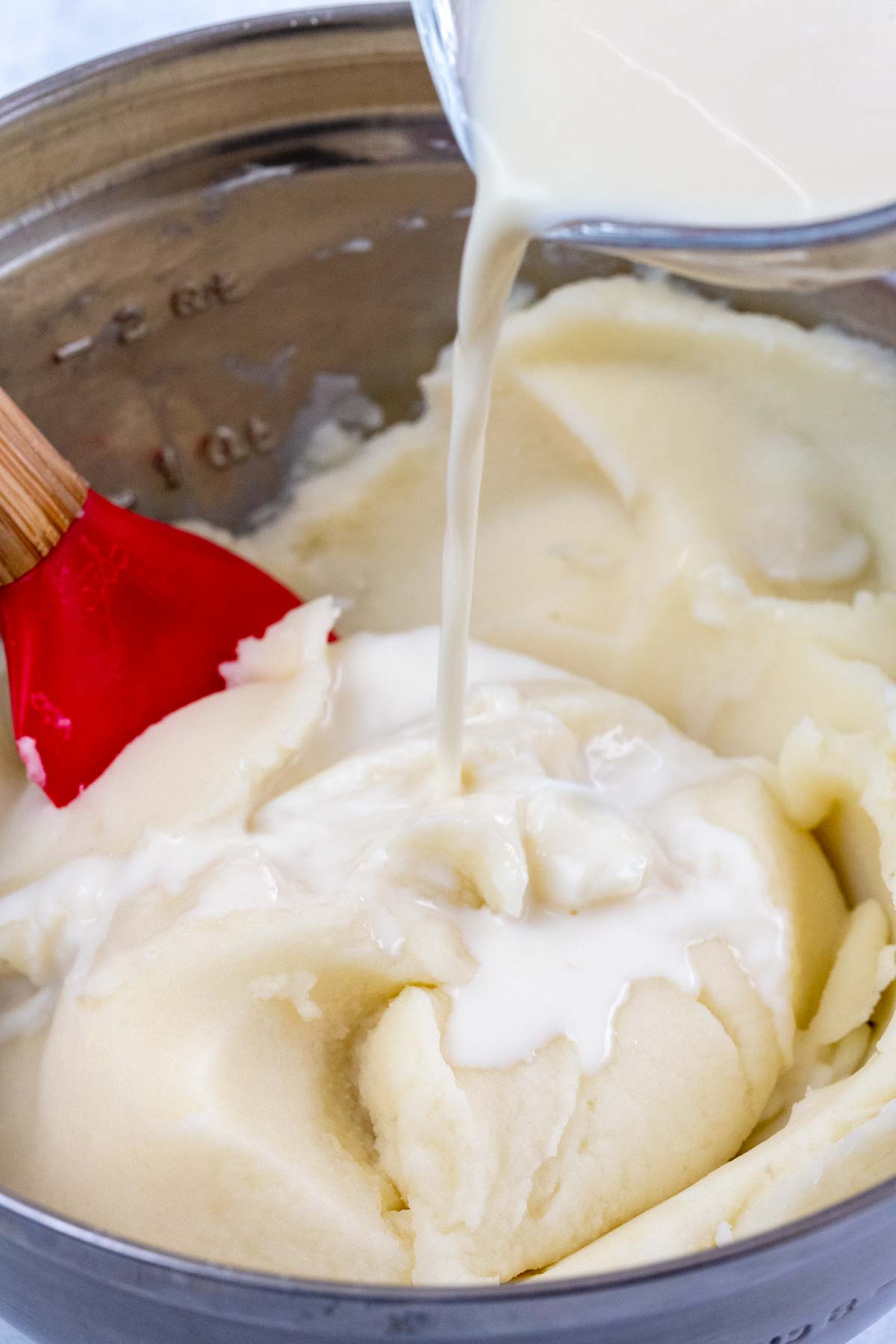 Milk being poured into a bowl of mashed potatoes.
