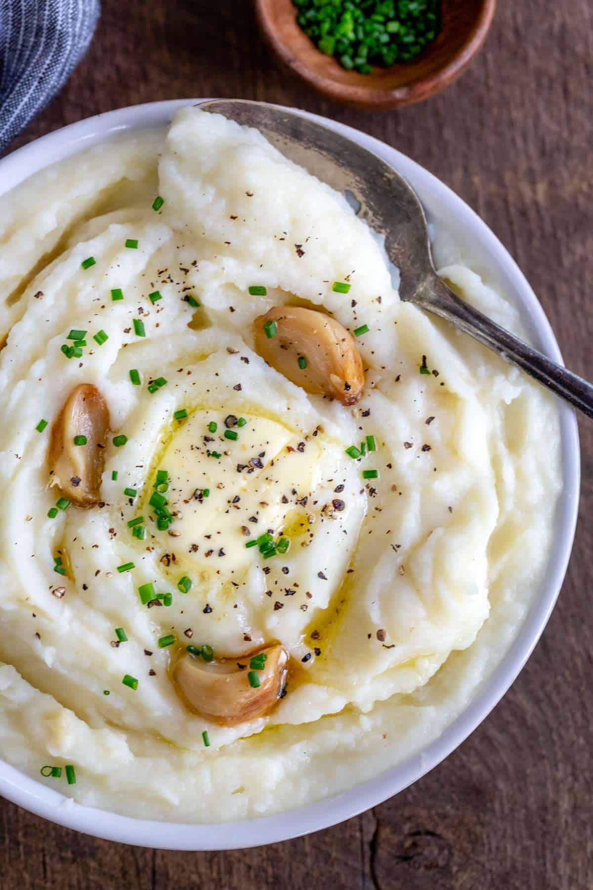 Bowl of mashed potatoes with three pieces of roasted garlic on top