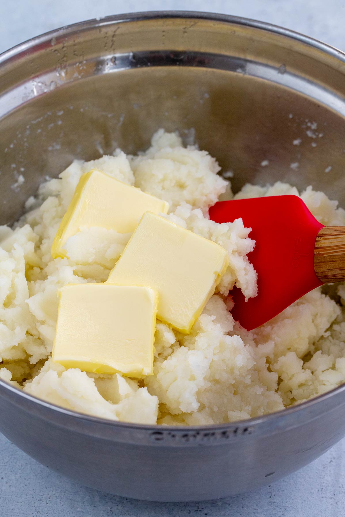Slices of butter in a mixing bowl of mashed potatoes.