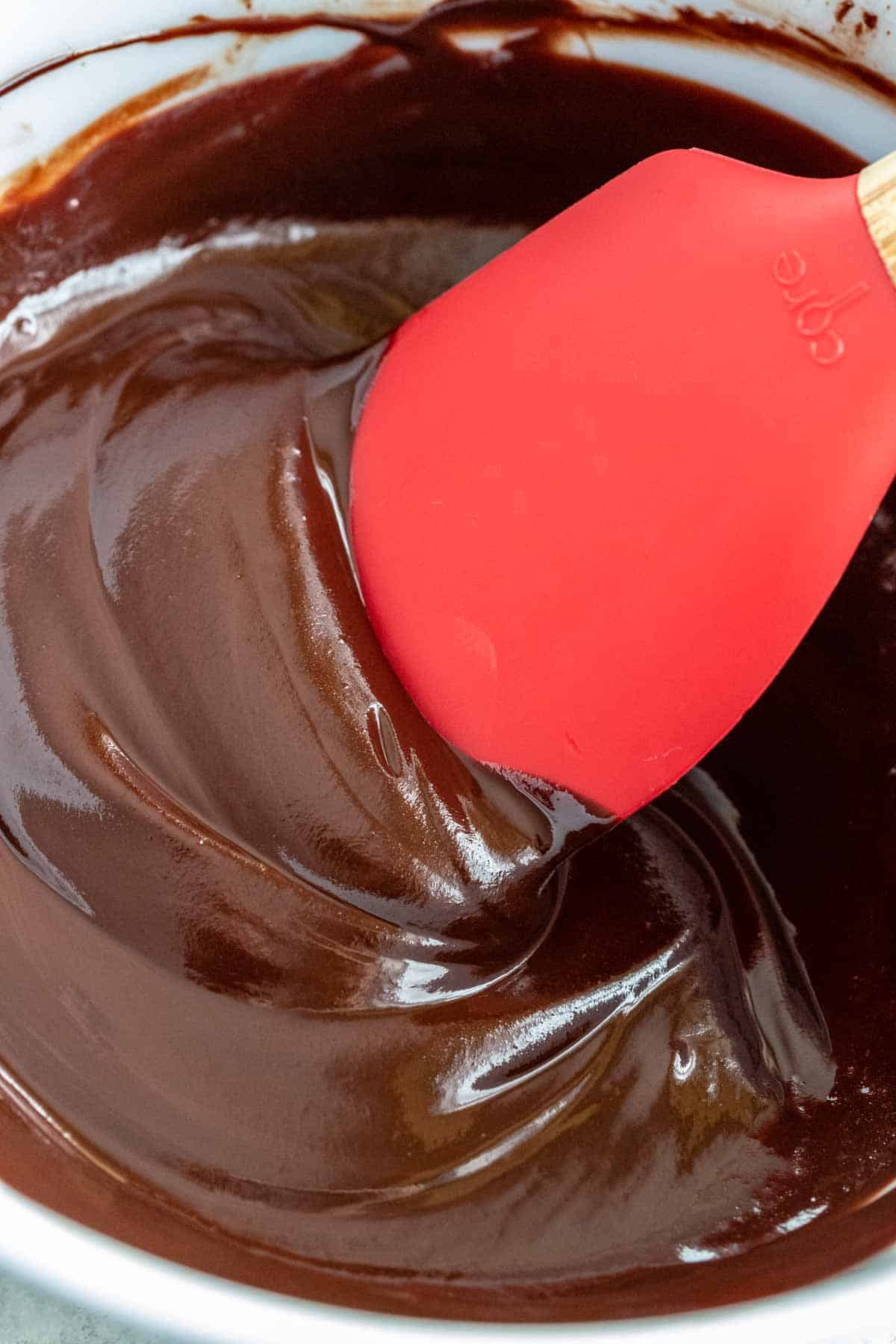 Red spatula mixing melted chocolate in a glass bowl.