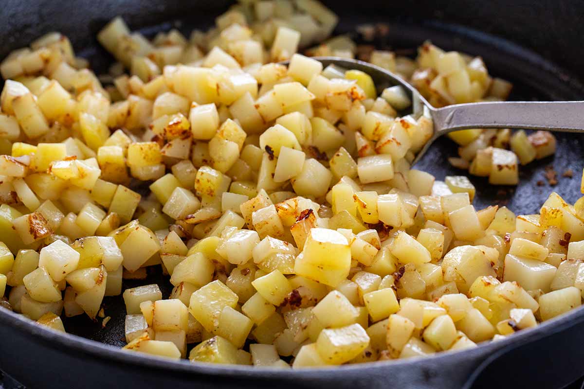 Cubes of potatoes sauteing in a cast iron skillet.