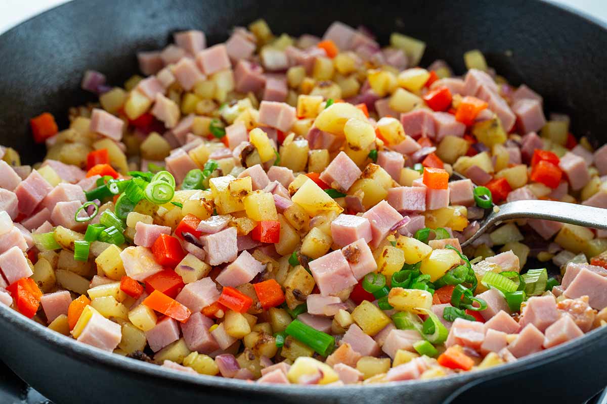 Sautéing cubes of ham, potatoes, and peppers in a cast iron skillet.