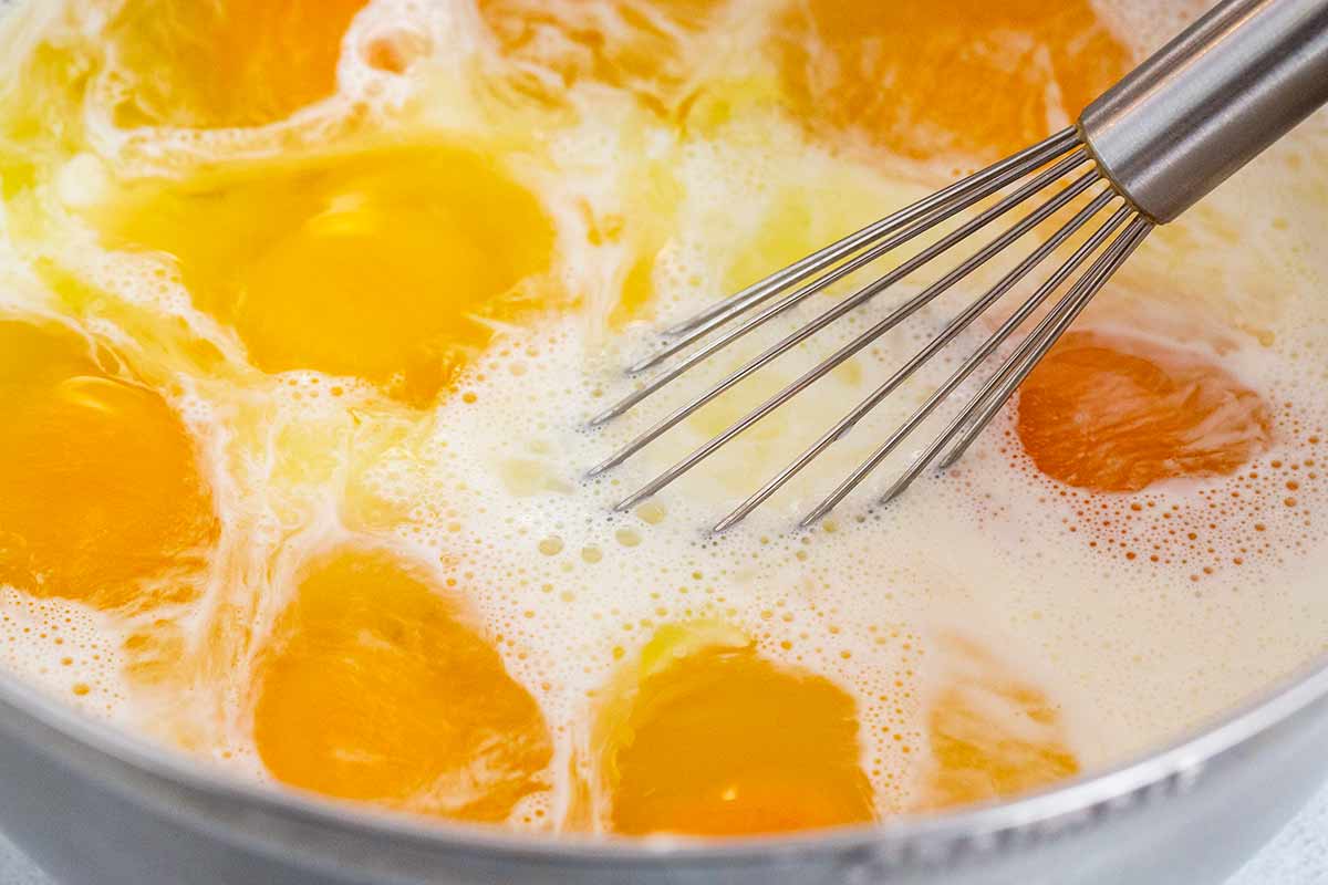 Whisk stirring a bowl of eggs and milk.