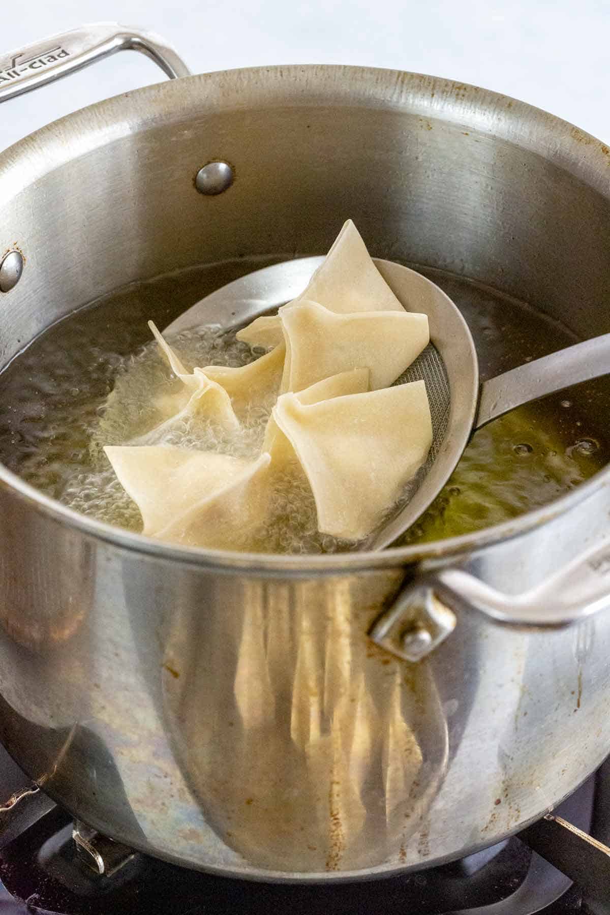 Lowering crab rangoon into hot oil with a spider strainer.